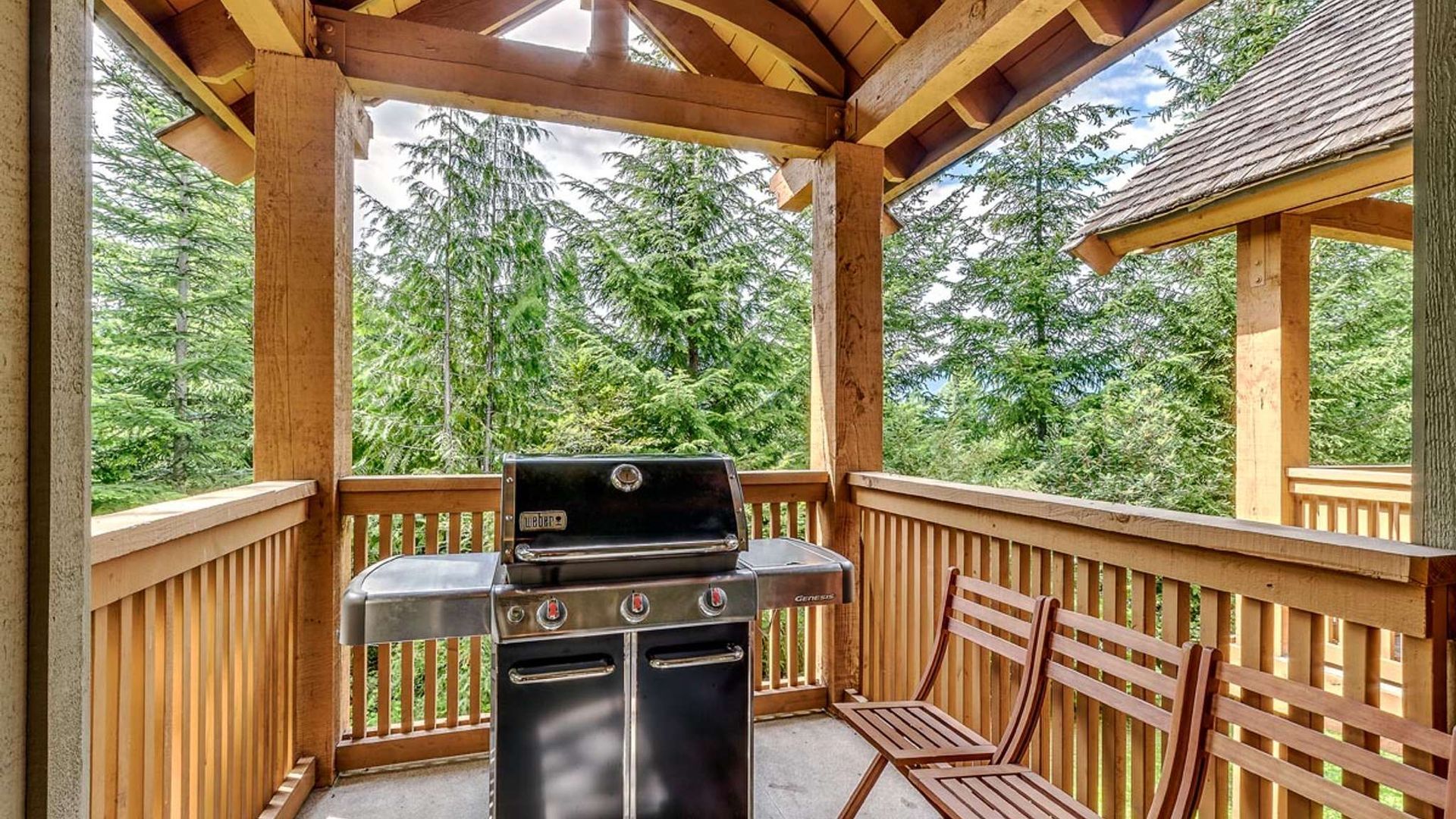 Covered wooden deck with a grill, bench, and forest view through open railings