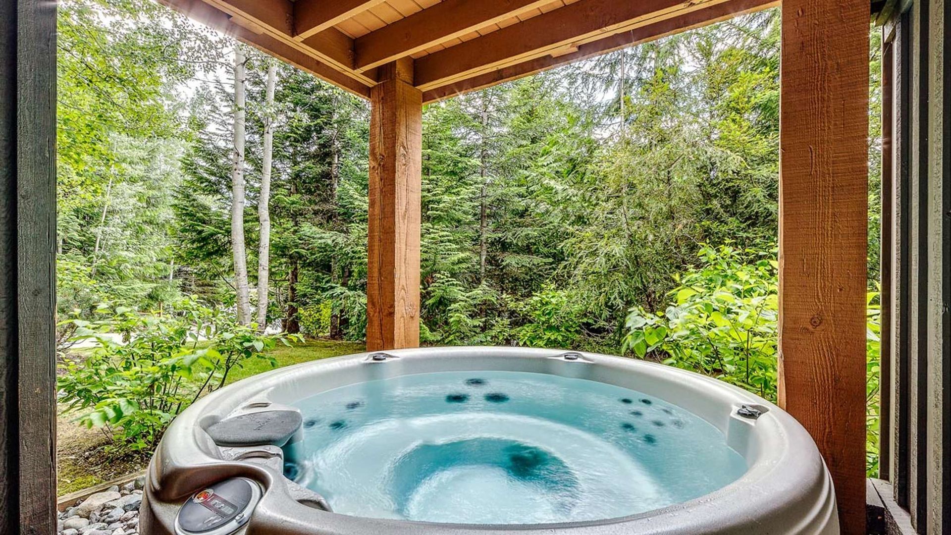 Hot tub on a covered wooden deck overlooking a lush green forest
