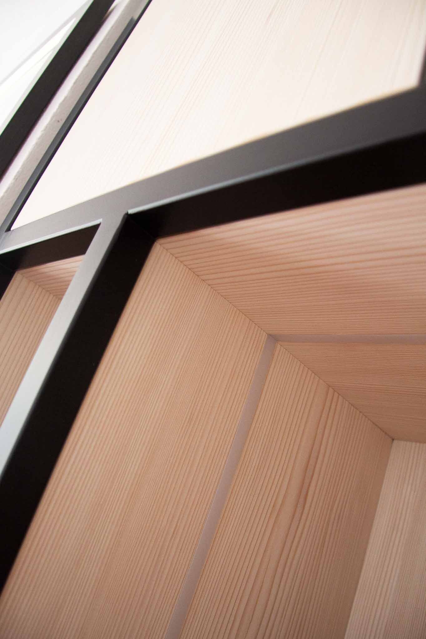 Nahaufnahme einer abgewinkelten Holzvertäfelung mit dunklem Metallrahmen.