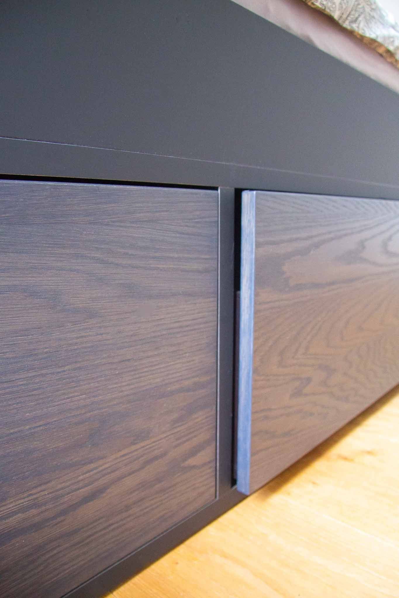 Zwei dunkle Holzschubladen unter einer dunkelgrauen Oberfläche, dazwischen ein vertikaler Griff auf einem hellen Holzboden.