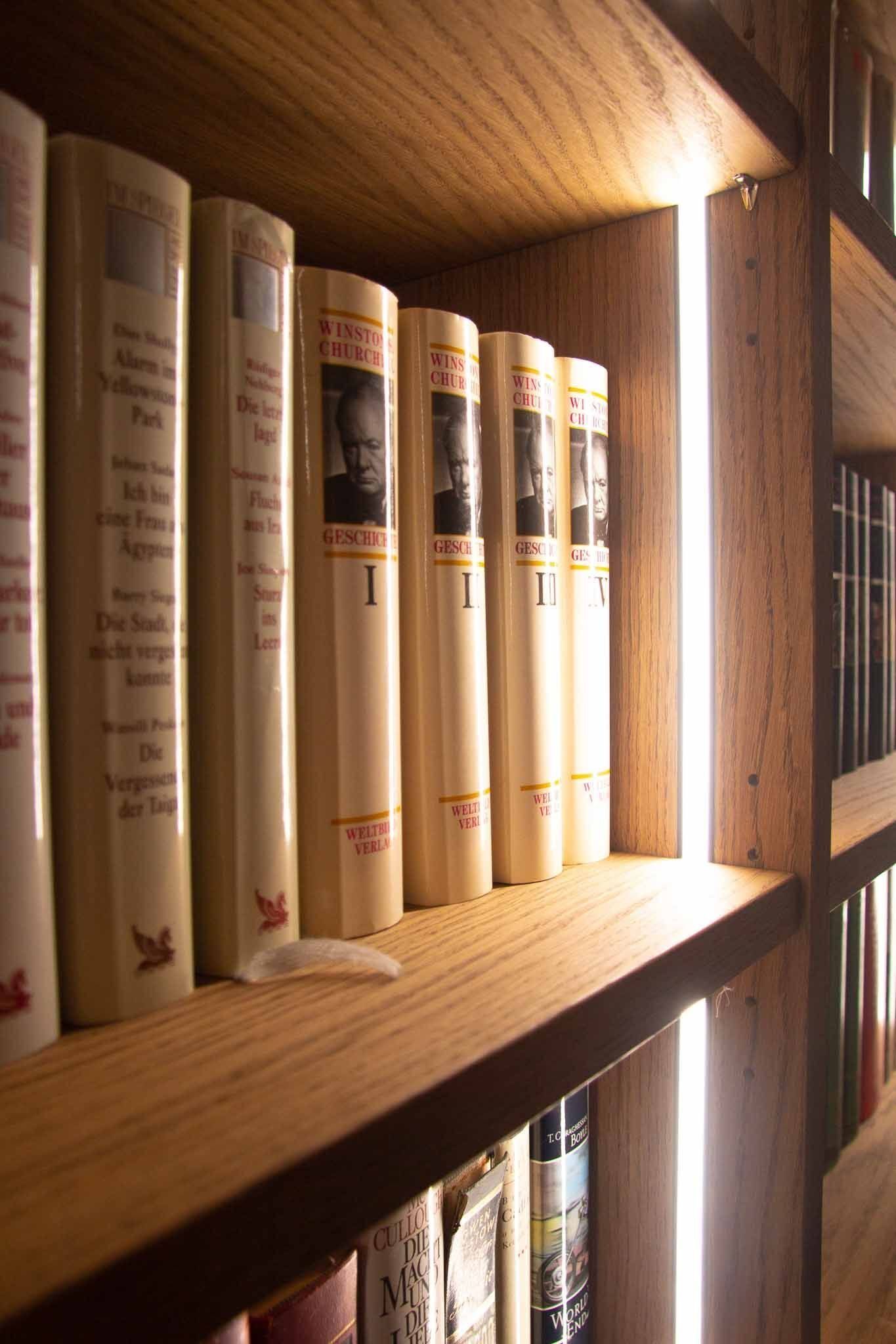 Bücher auf einem Holzregal, warme Beleuchtung, Buchrücken sichtbar.