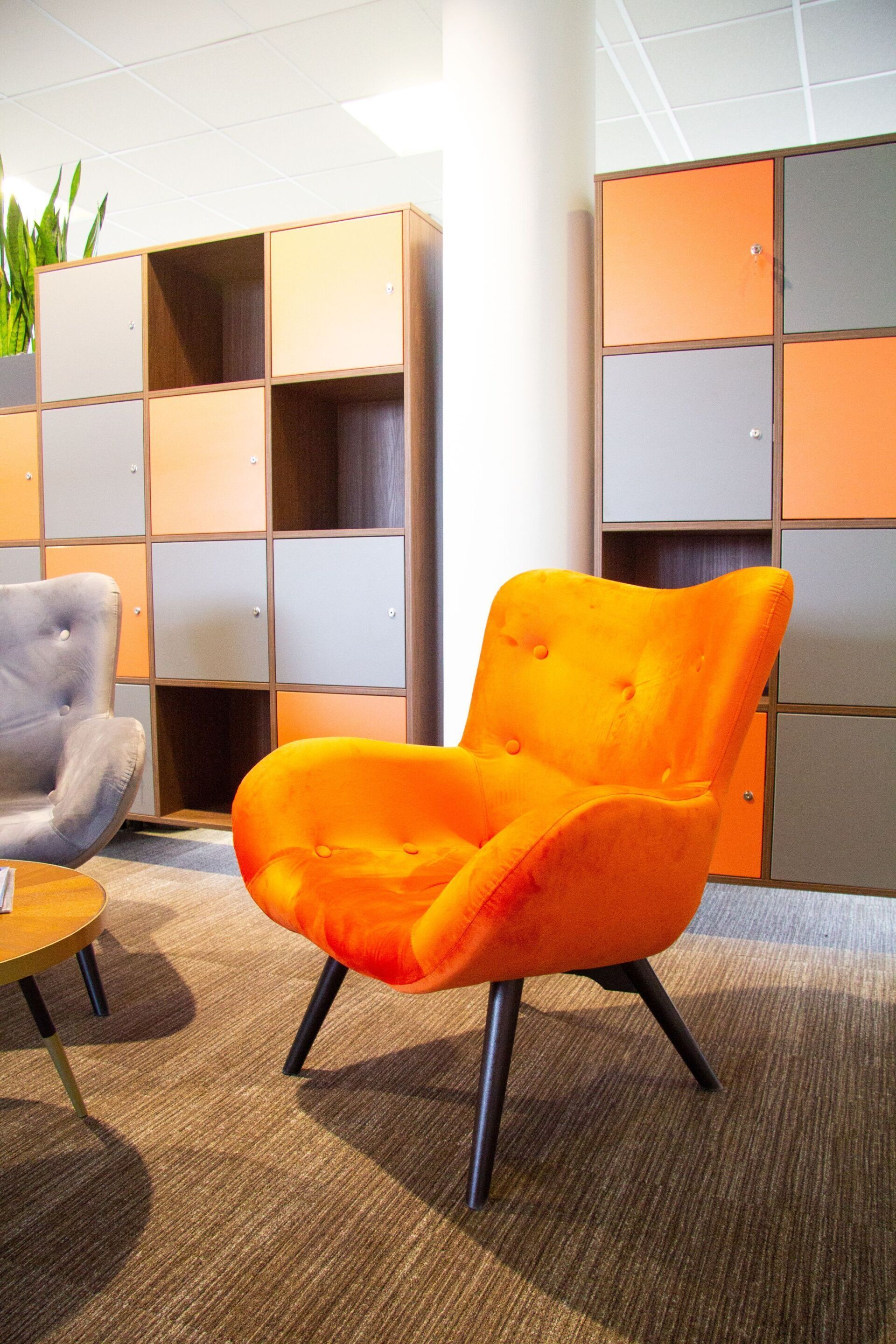 Orangefarbener Samtstuhl in einem modernen Büroumfeld mit farbenfrohen Aufbewahrungseinheiten.