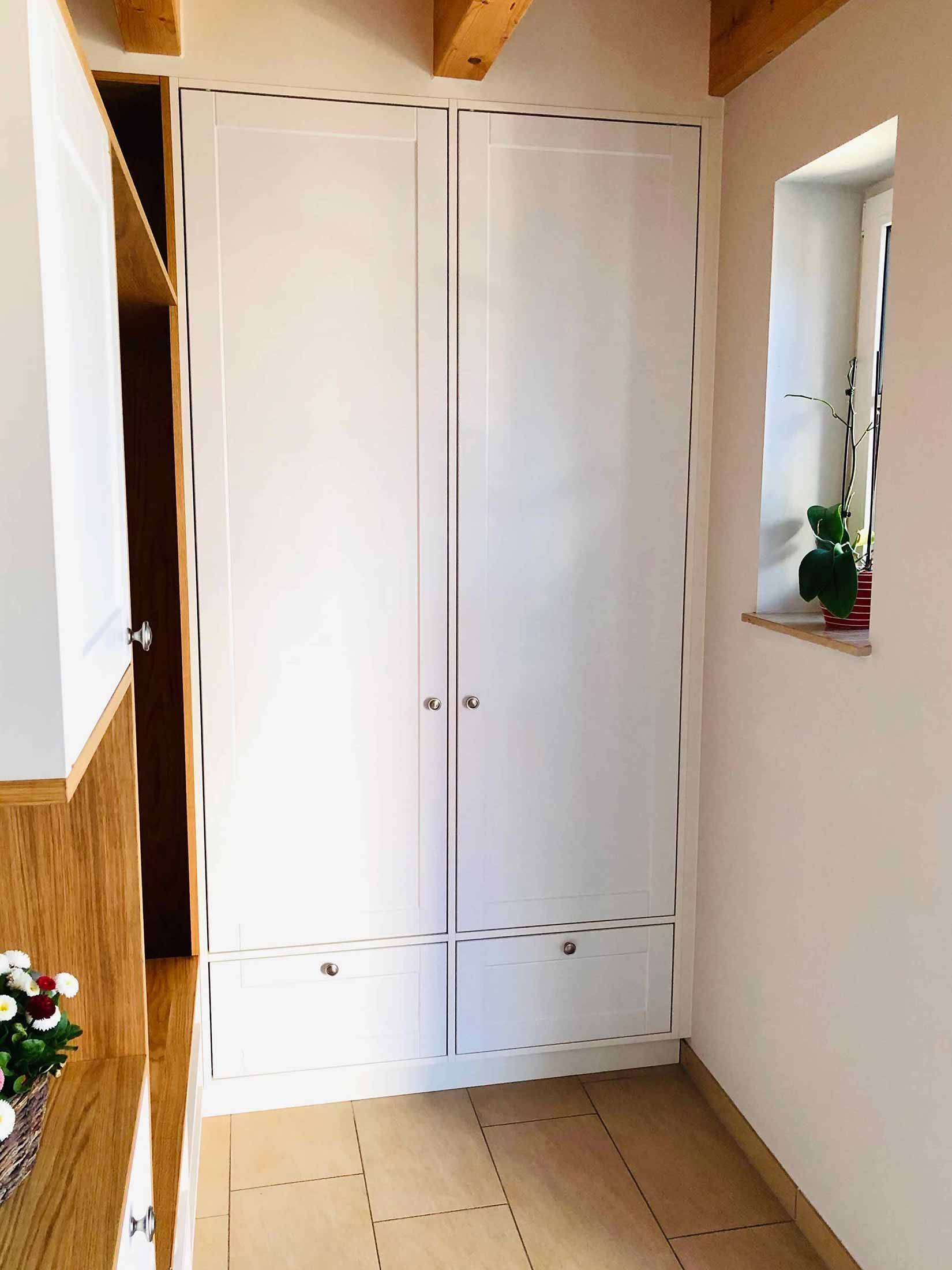 Weißer Schrank mit zwei Türen und zwei Schubladen in einem Flur.