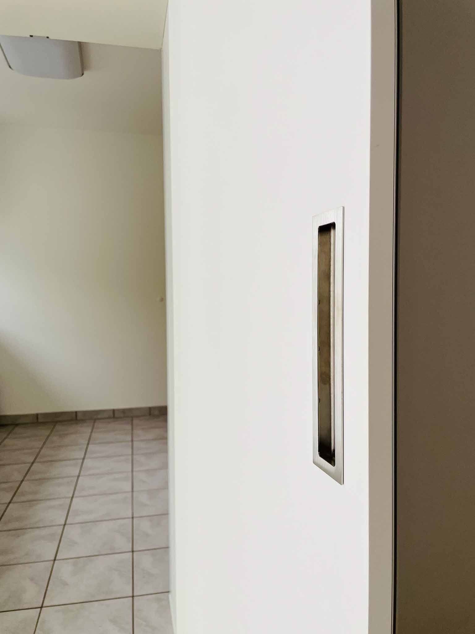 Weiße Wand mit rechteckiger Griffmulde, Türöffnung zu einem Raum mit Fliesenboden.