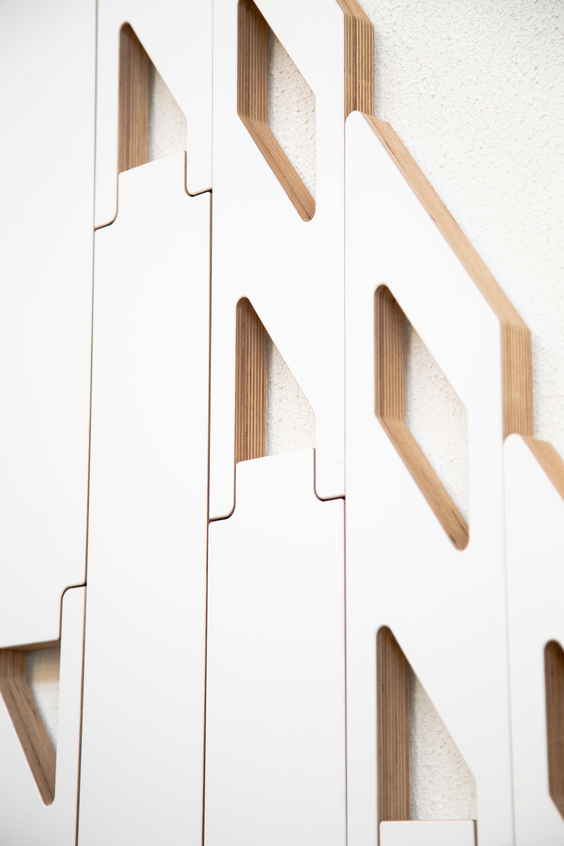Weiße Paneele mit Rautenausschnitten greifen ineinander und werden an einer weißen Wand montiert, wodurch ein geometrisches Muster entsteht.