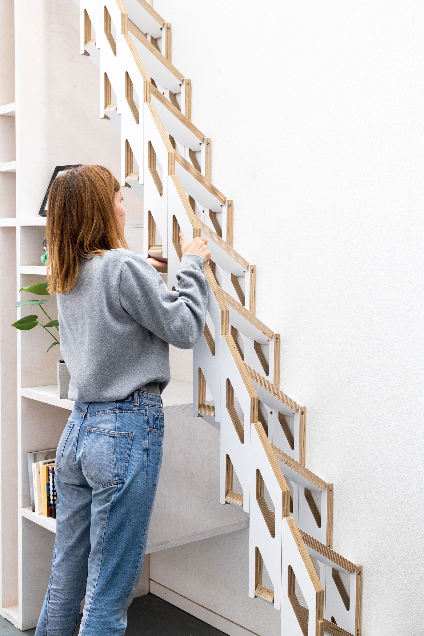 Frau montiert eine weiße Klapptreppe. Sie steht an einer Wand, in deren Nähe Bücherregale stehen.