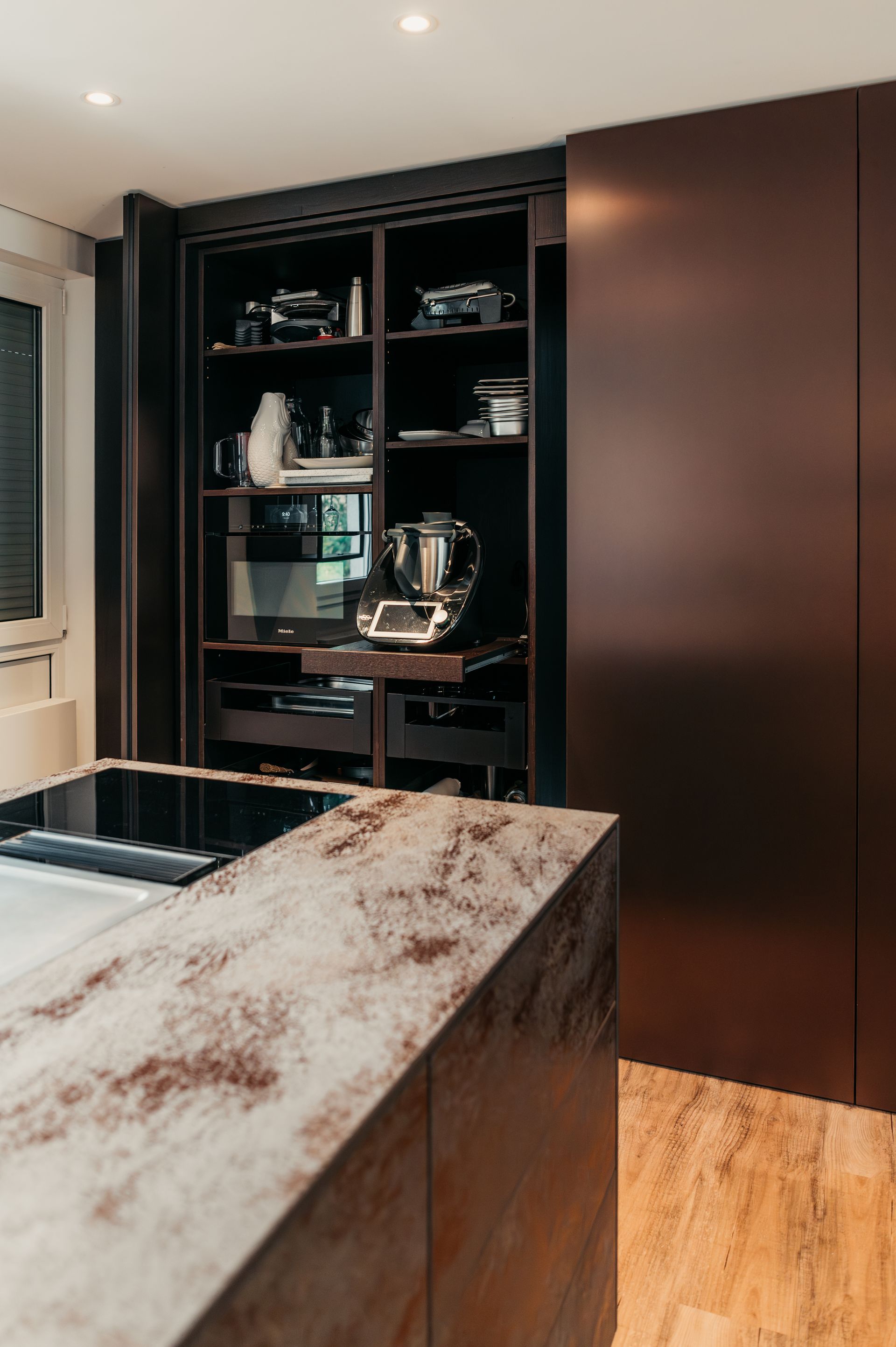 Moderne Küche mit braunen Schränken und einem offenen Regal mit Geräten.