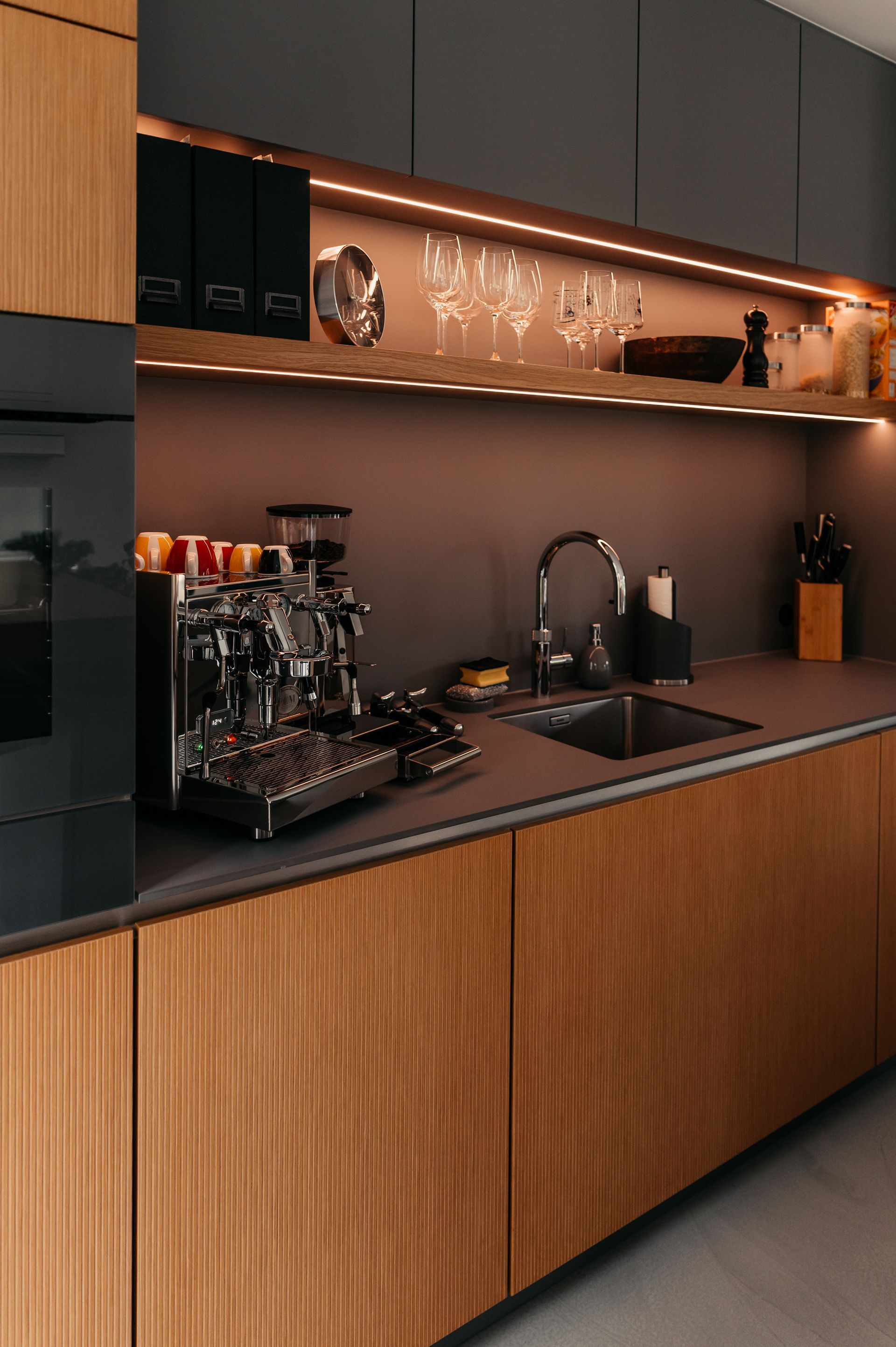 Moderne Küche mit Holzschränken, Espressomaschine und Glaswaren auf einem Regal mit Lichtleisten.