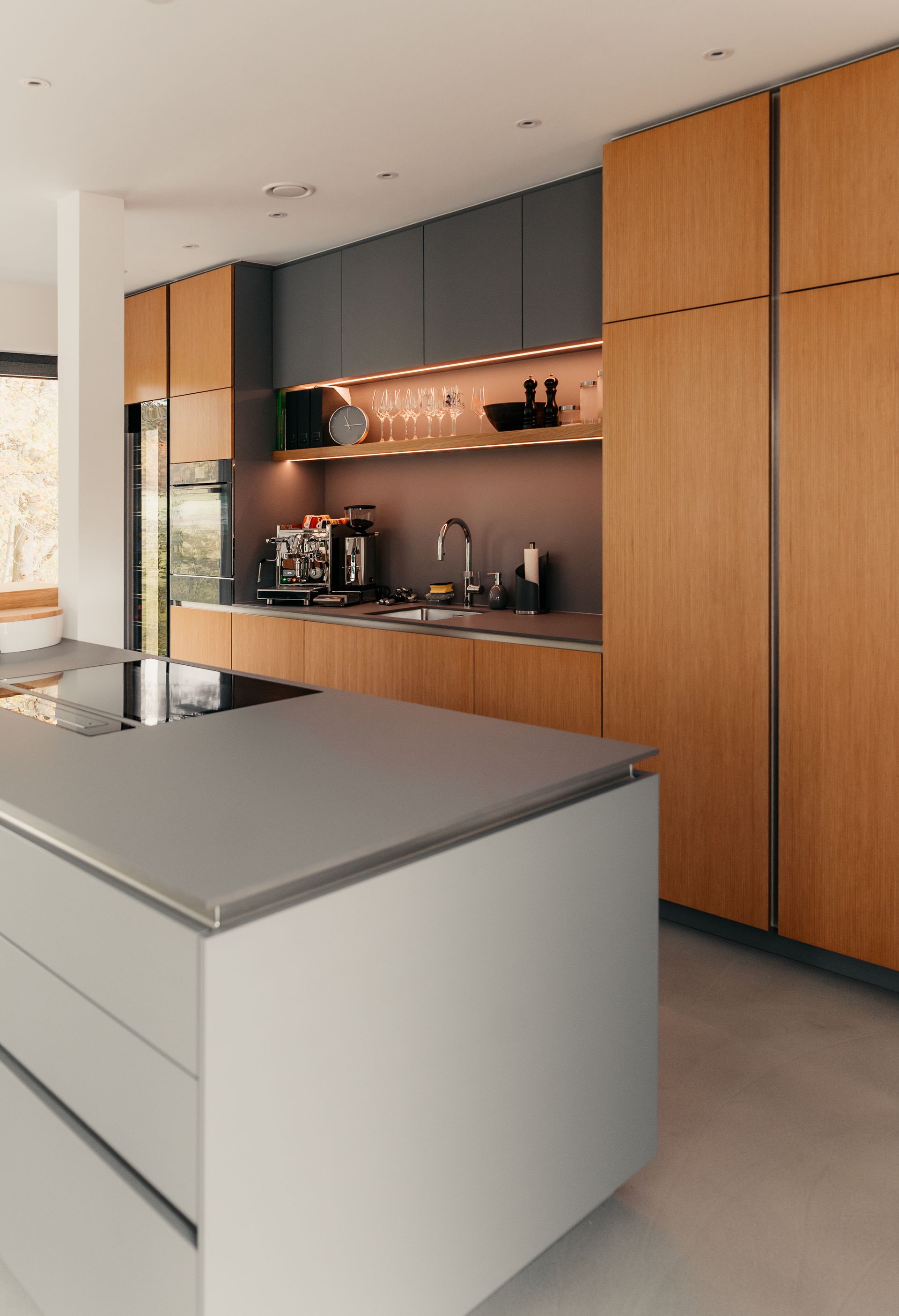 Moderne Küche mit Holzschränken, grauen Arbeitsplatten und einer Kochinsel.