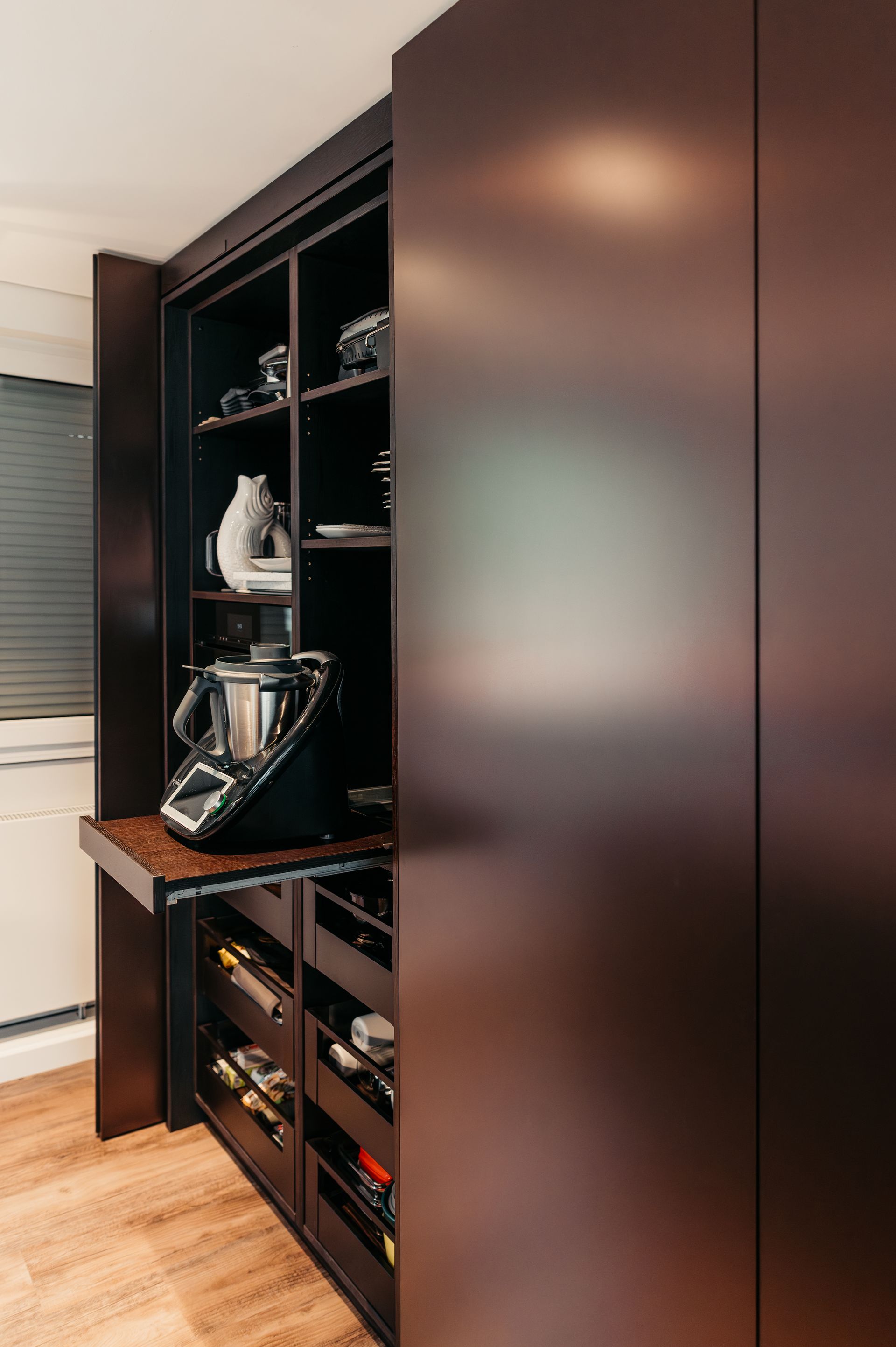 Vorratsschrank aus dunklem Holz mit ausziehbarem Regal für Küchengeräte, Regalen und Schubladen.