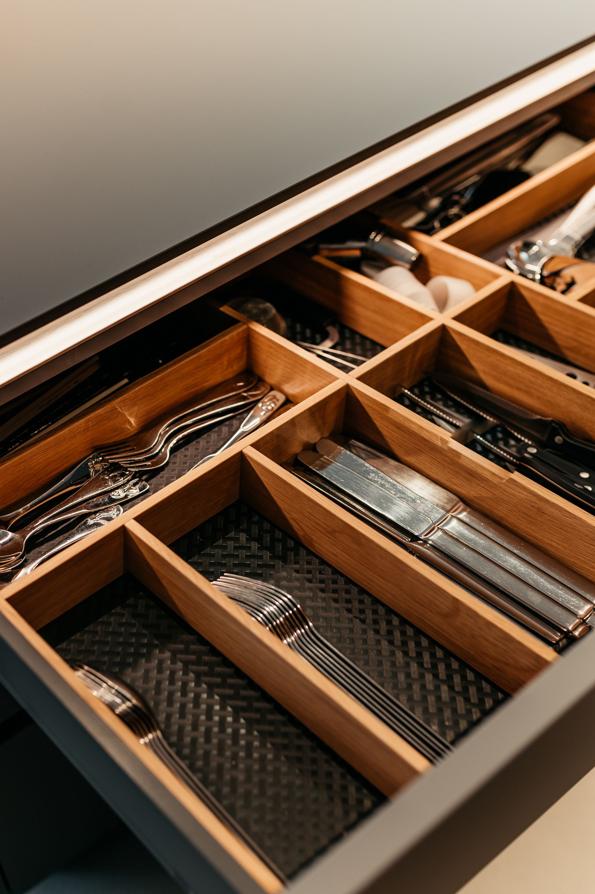 Silberbesteck ordentlich angeordnet in einer Holzschublade mit schwarzem Innenleben.