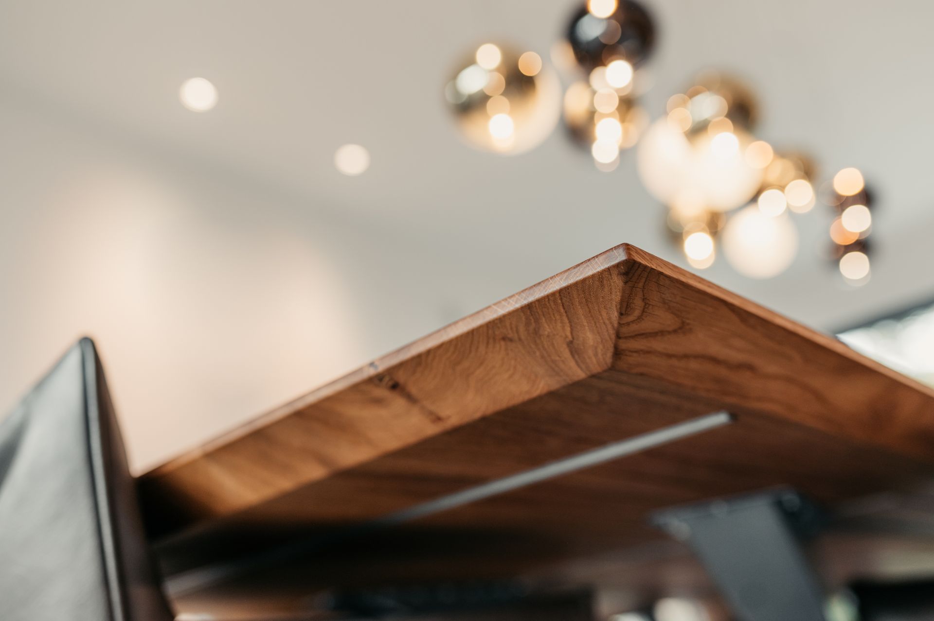 Nahaufnahme einer braunen Holztischkante mit Metallstütze, unscharfer Hintergrund mit Lichtern.