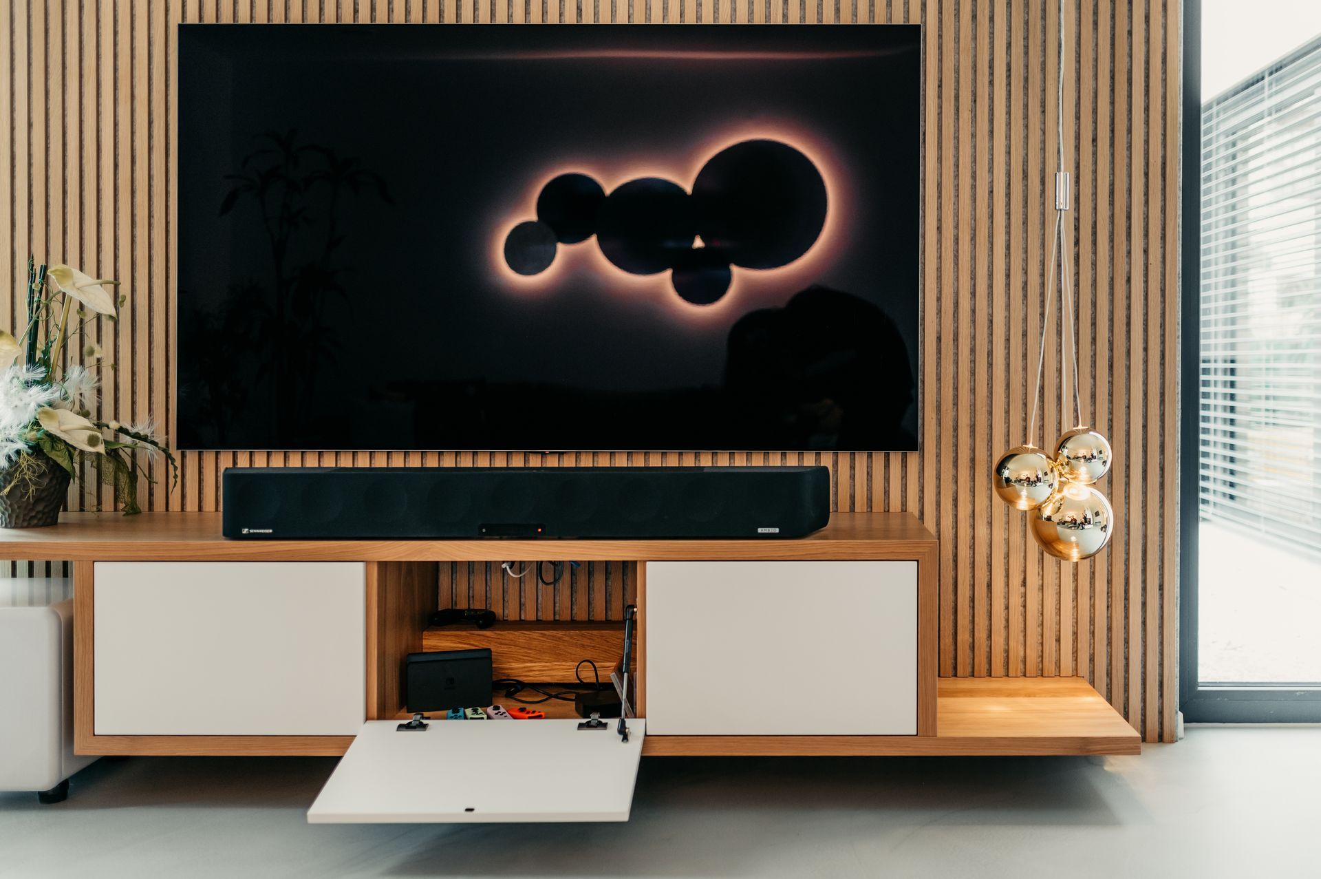 TV-Setup: schwarzer Bildschirm mit leuchtenden Kreisen, Soundbar, Schrank mit offener Tür, Holzvertäfelung.