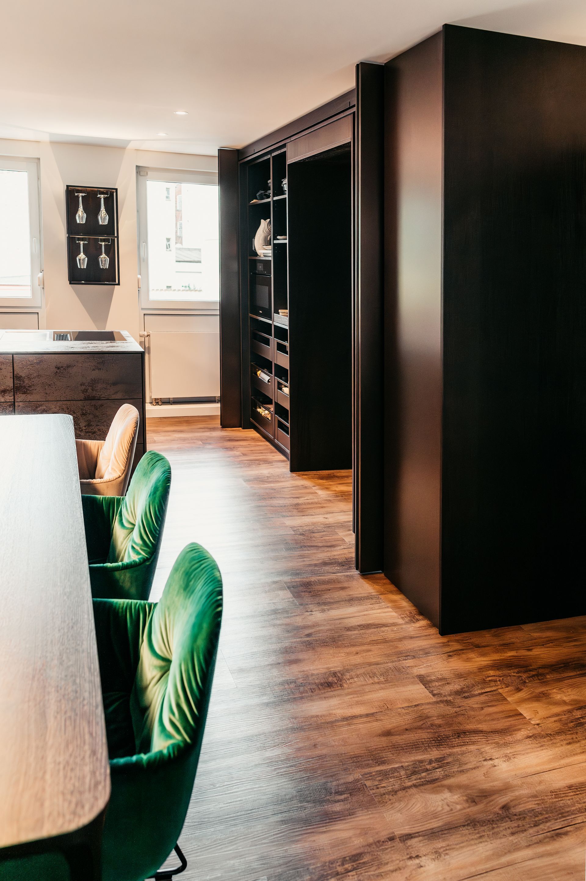 Grüne Esszimmerstühle aus Samt neben einem Holzboden und dunklen Schränken.