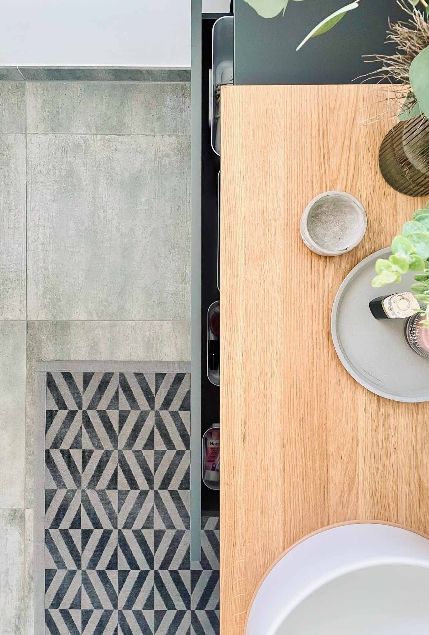 Holztisch mit grauem Teller, kleiner Schüssel und Blumen; gemusterter Teppich und Steinboden.