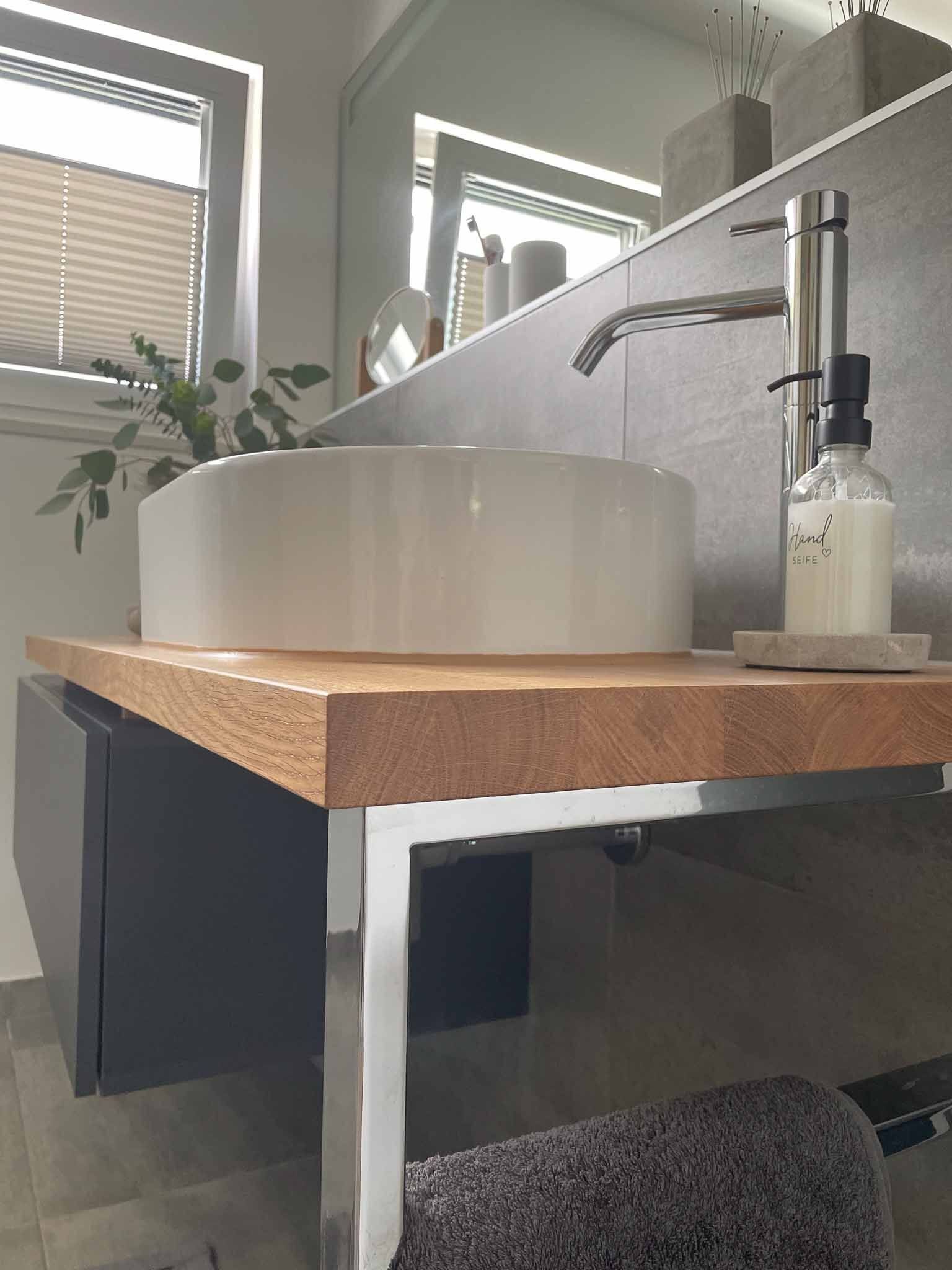 Modernes Badezimmer mit einem weißen Waschbecken auf einer Holzplatte, Beinen aus Edelstahl und einem schwarzen Schrank.