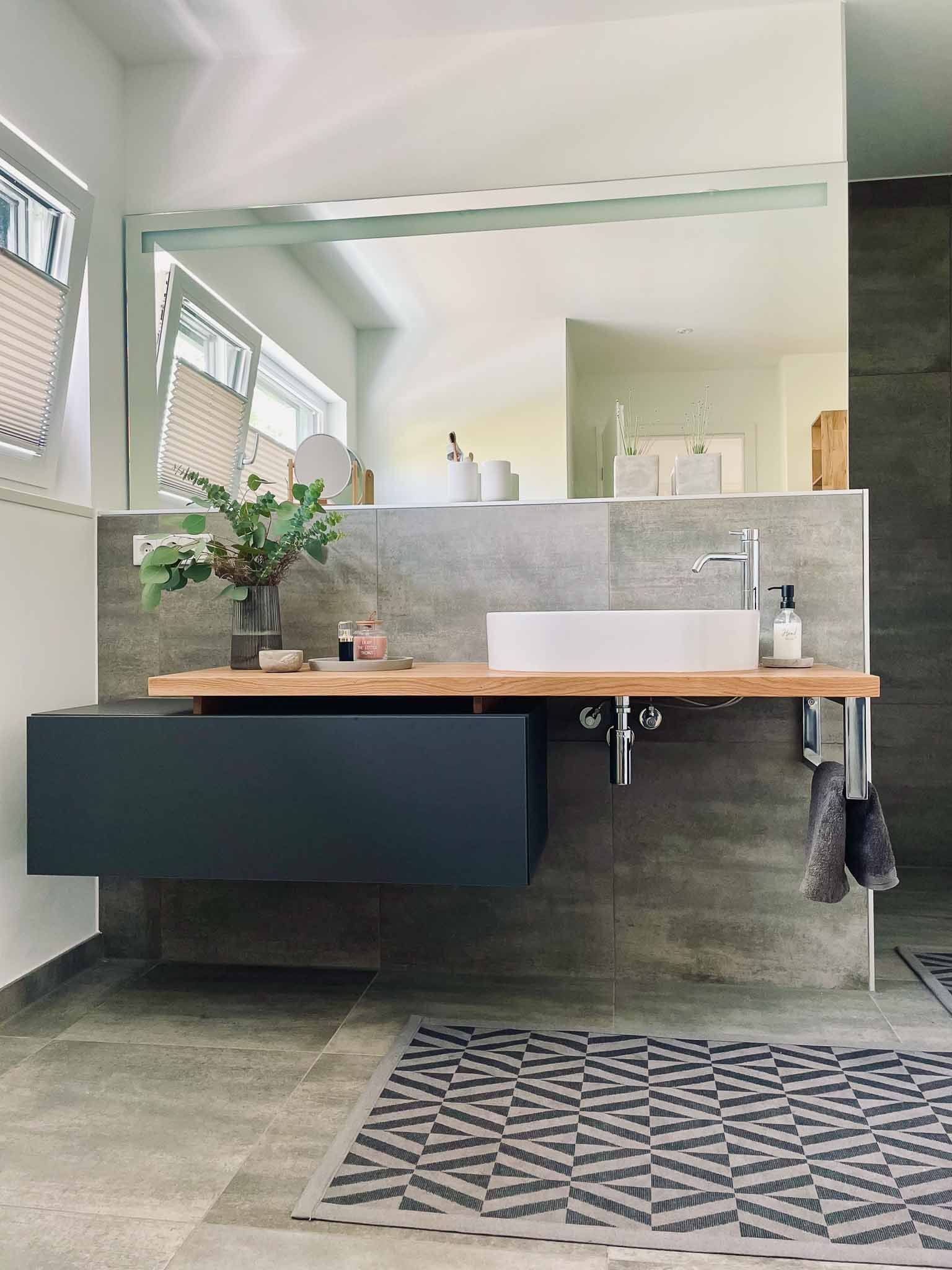 Modernes Badezimmer mit schwebendem Waschtisch, grauem Schrank, Holzregal, weißem Waschbecken und Spiegel.