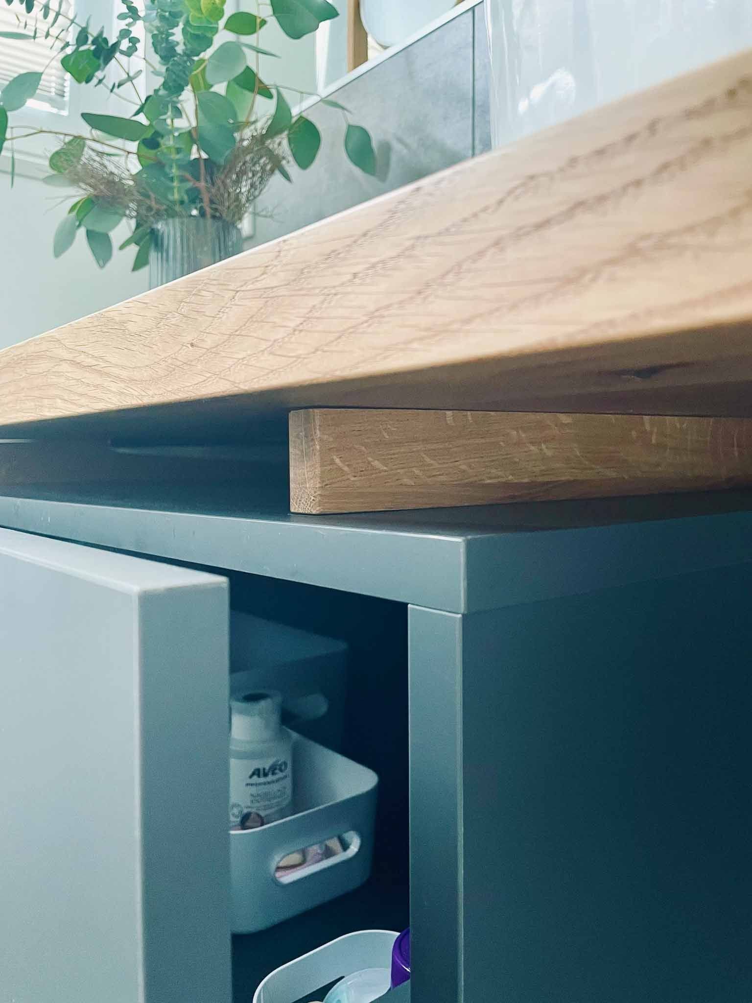 Badezimmerwaschtisch mit offenem grauen Schrank, Holztheke und Blumenarrangement.