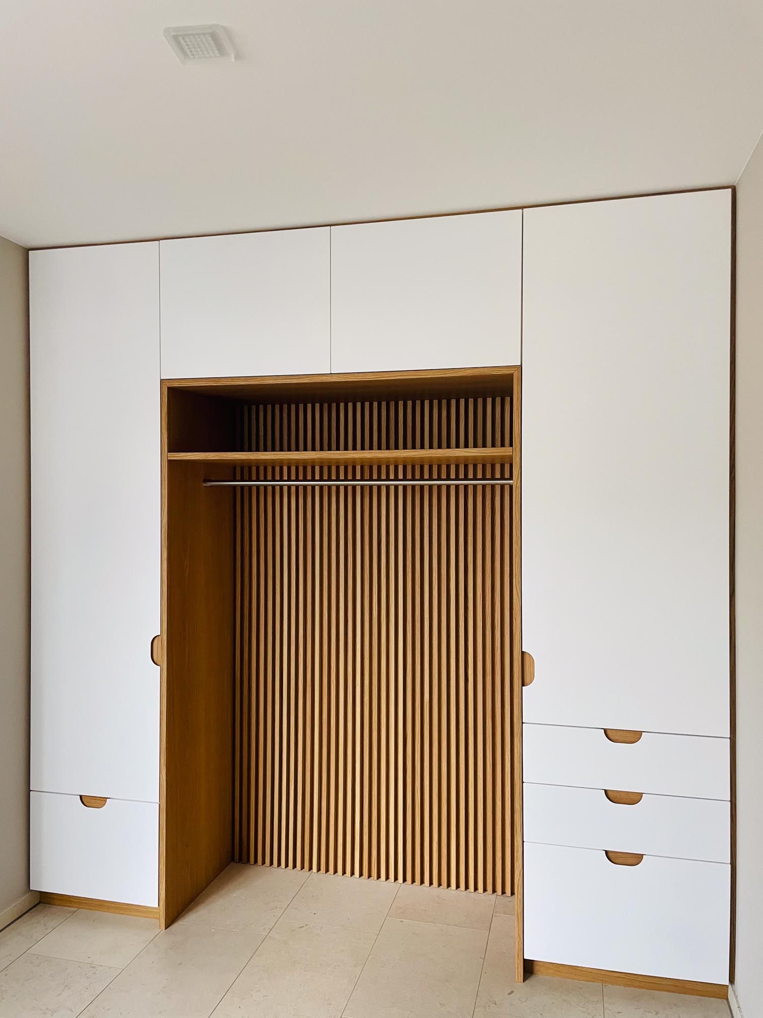Weißer Einbauschrank mit Holzlattenrückwand und Schubladen. Offener Bereich mit Kleiderstange.