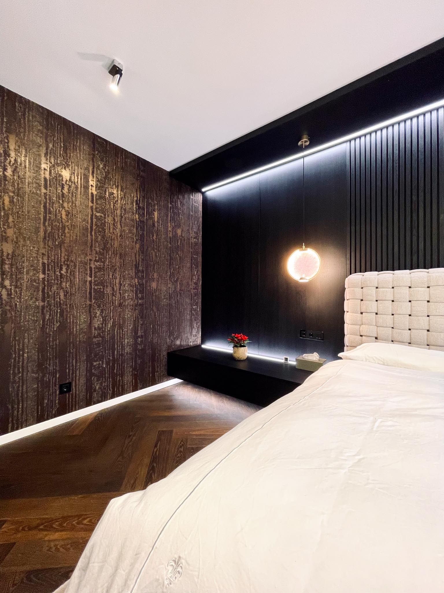 Schlafzimmer mit strukturierter Tapete, schwarzer Akzentwand, schwebendem Regal und einem Bett mit weißer Bettwäsche.