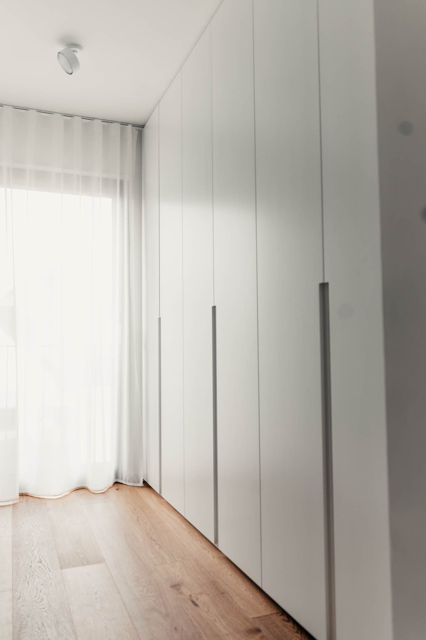 Weiße Schranktüren säumen einen Raum mit einem Fenster und durchsichtigen Vorhängen.
