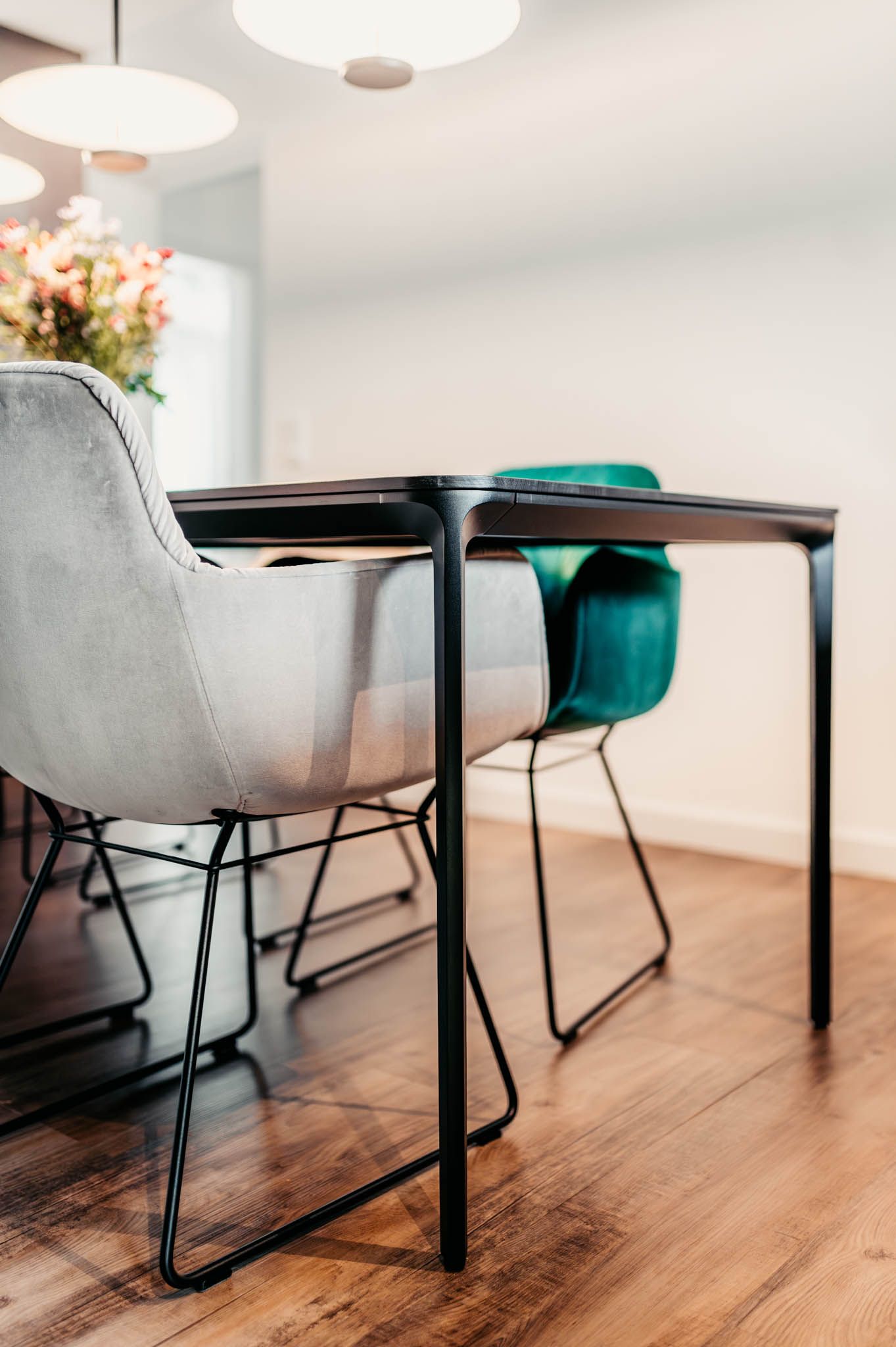 Esstisch mit schwarzem Gestell, moderne Stühle in Grau und Blaugrün, auf einem Holzboden.