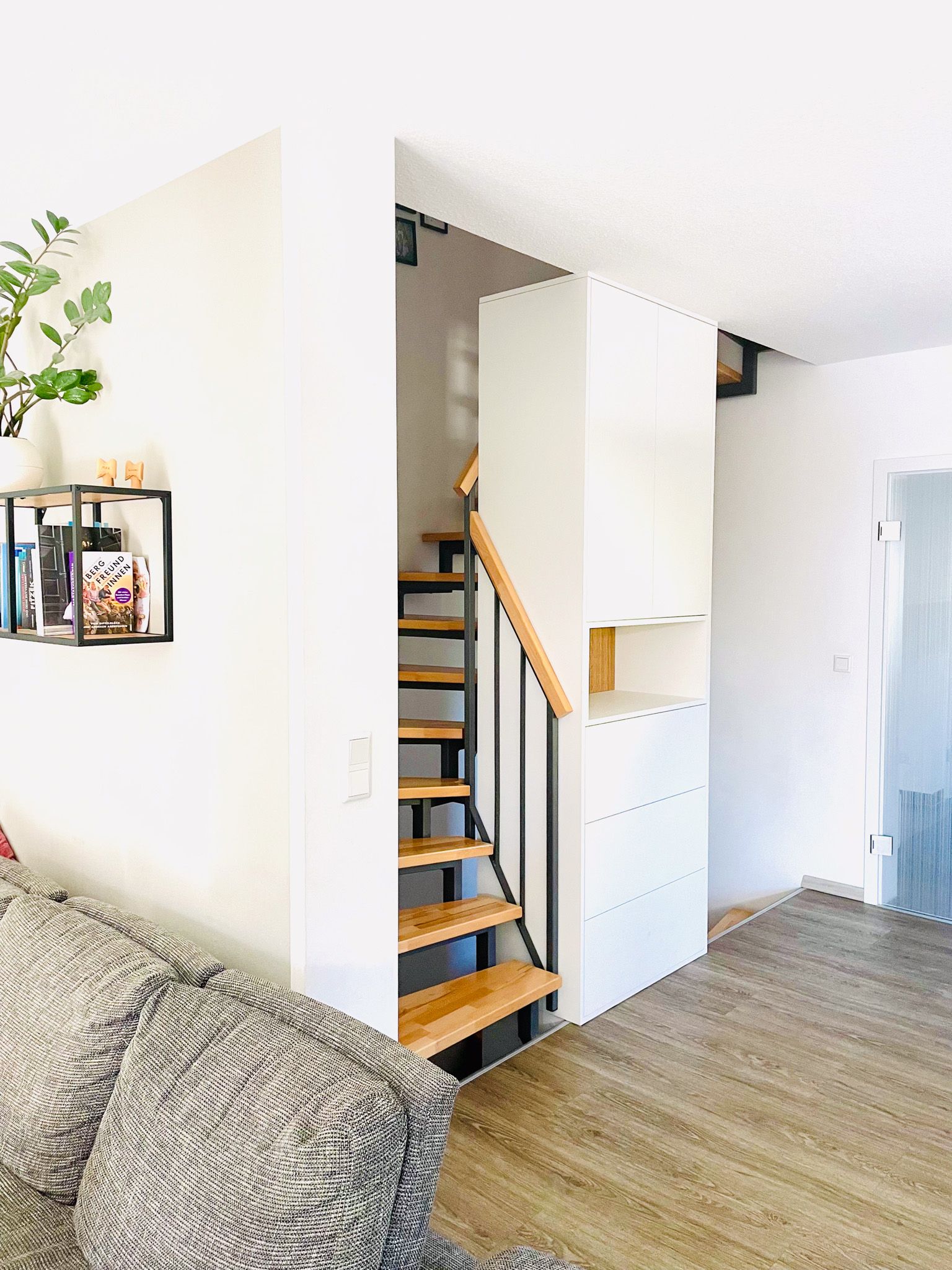 Treppe mit Holzstufen, schwarzem Geländer und weißem Stauraum. Neben der Treppe befindet sich eine weiße Wand.