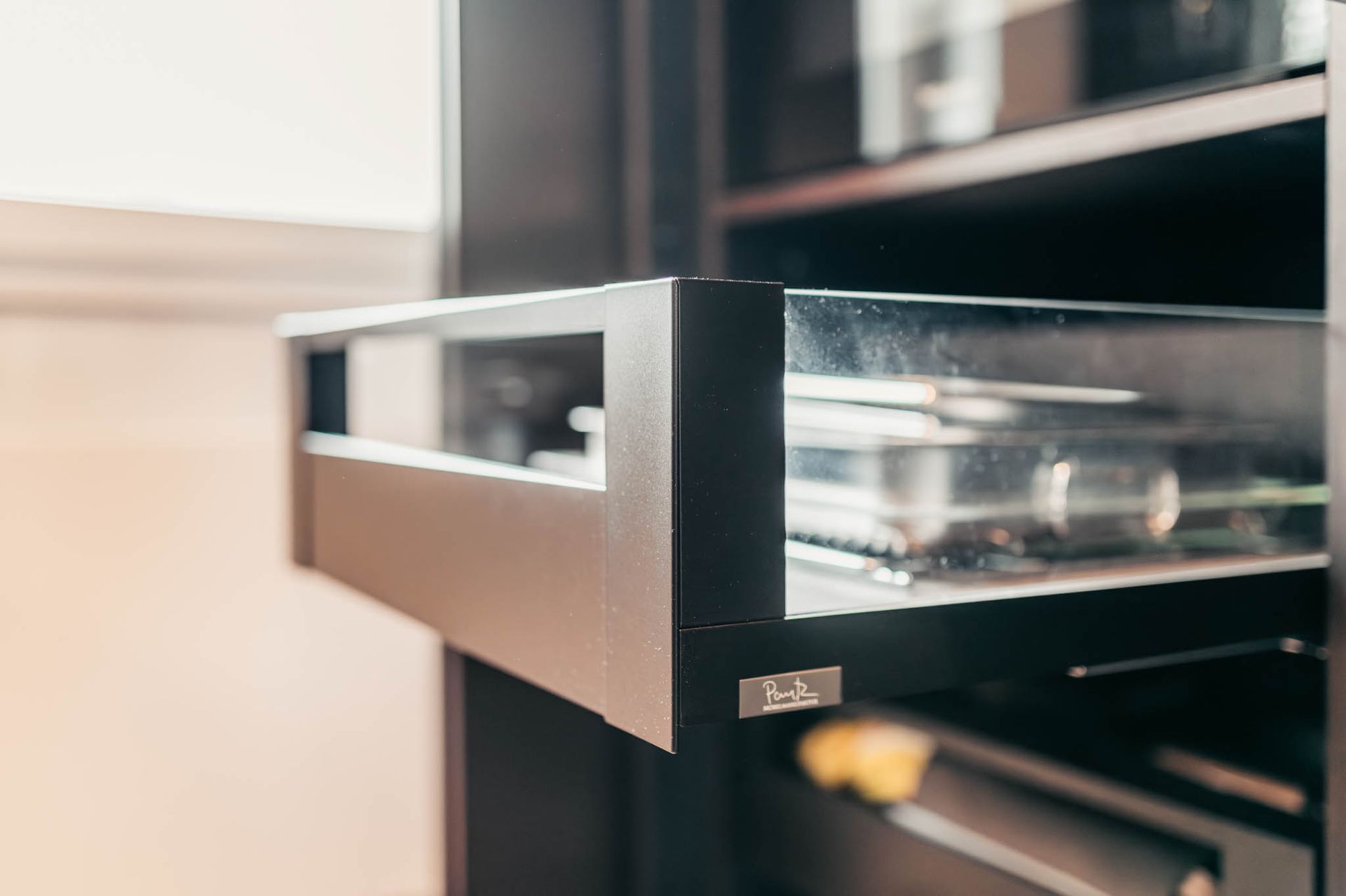 Aufgezogene schwarze Schrankschublade mit Glasgefäßen, in einem durch ein Fenster beleuchteten Raum aufgestellt.
