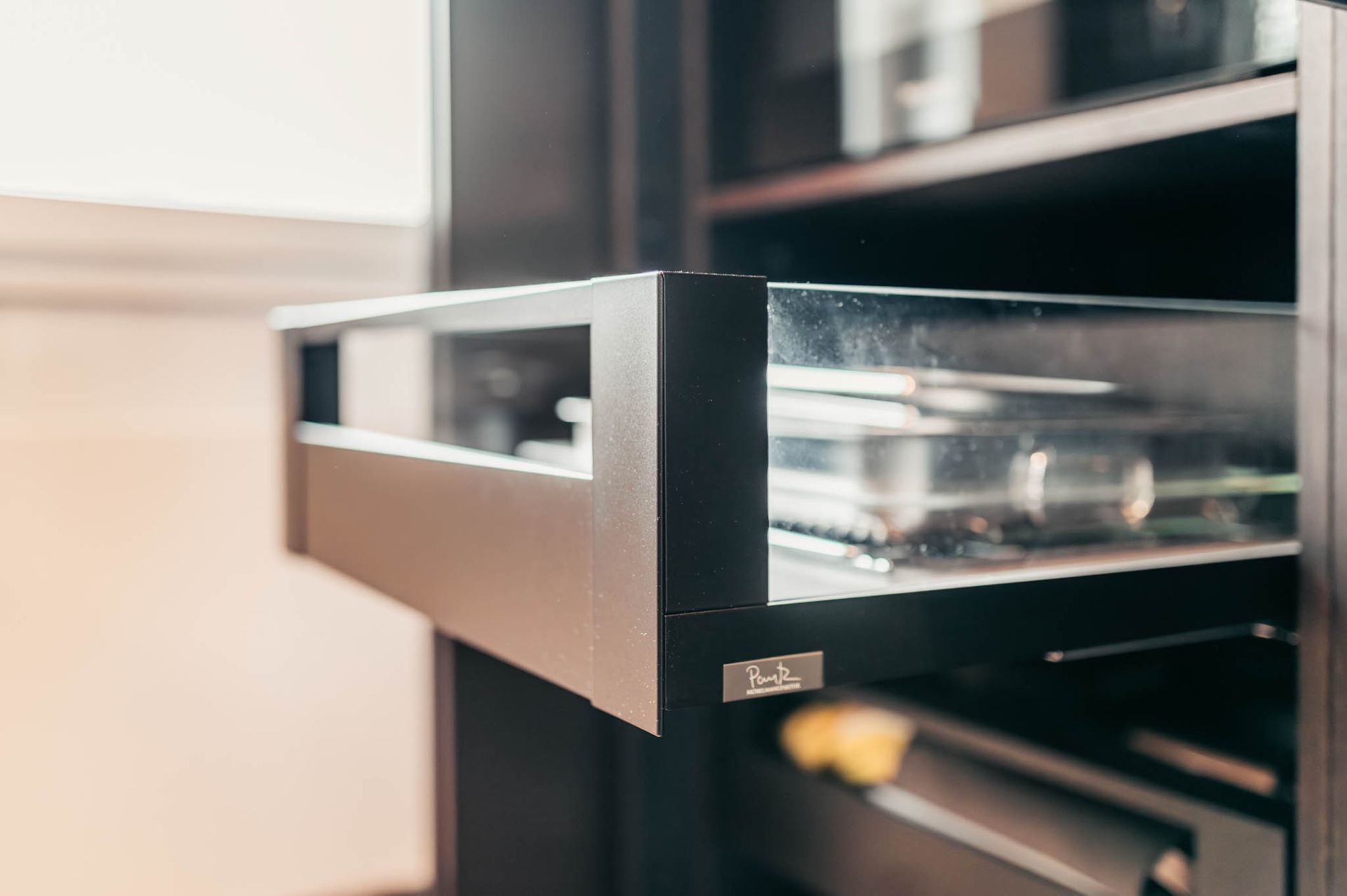 Nahaufnahme einer teilweise geöffneten dunklen Schrankschublade mit Glasseiten, die metallische Gegenstände enthält.