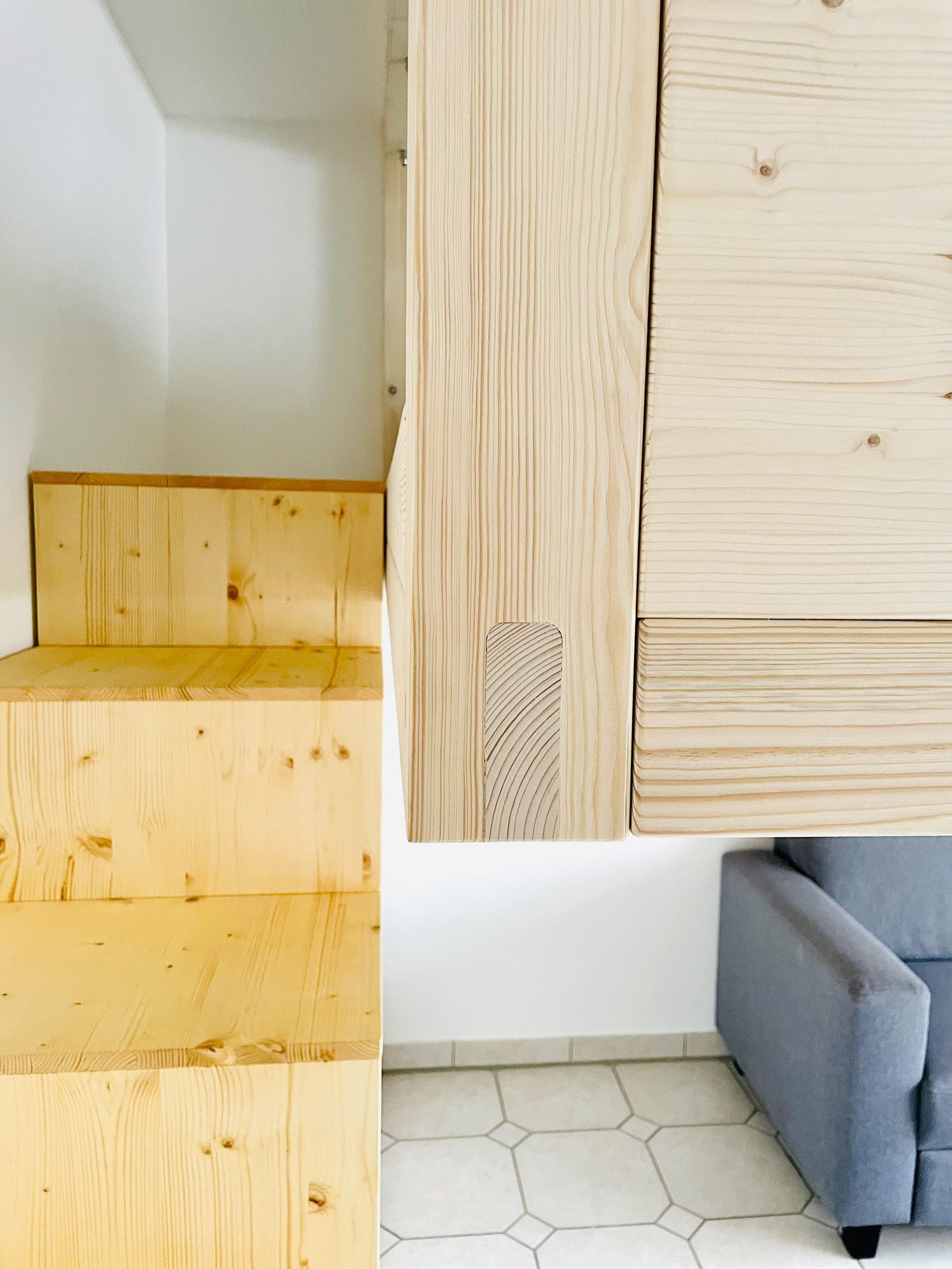 Nach oben führt eine Holztreppe mit einem passenden Holzschrank und einem grauen Sofa.