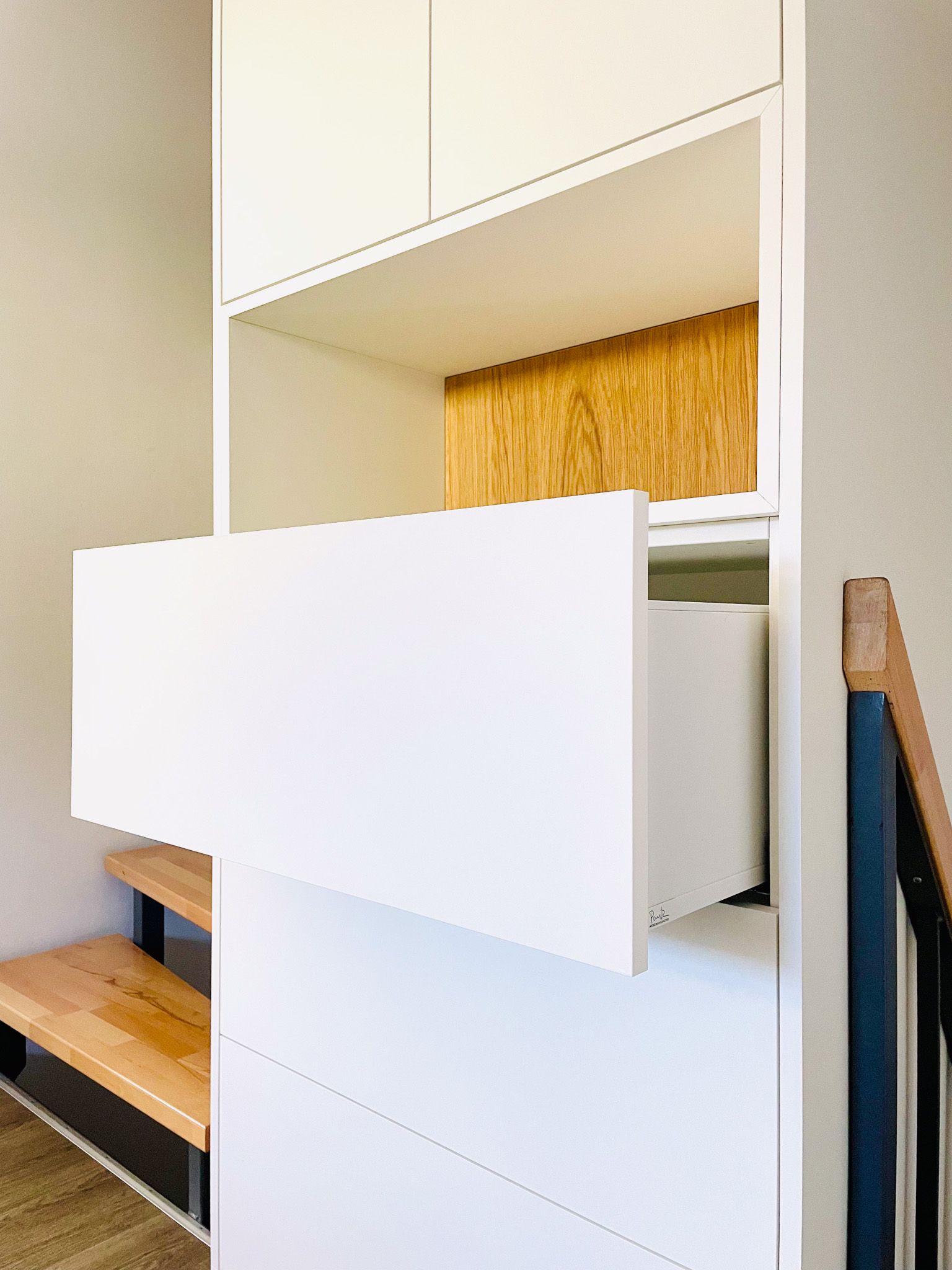 Weißer Schrank mit einer offenen Schublade, in eine Treppenhauswand eingebaut; Innenausstattung aus Holz.