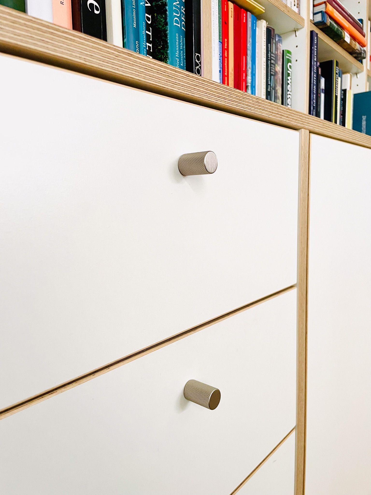 Weiße Schubladen mit strukturierten Knöpfen, Teil eines eingebauten Bücherregals.