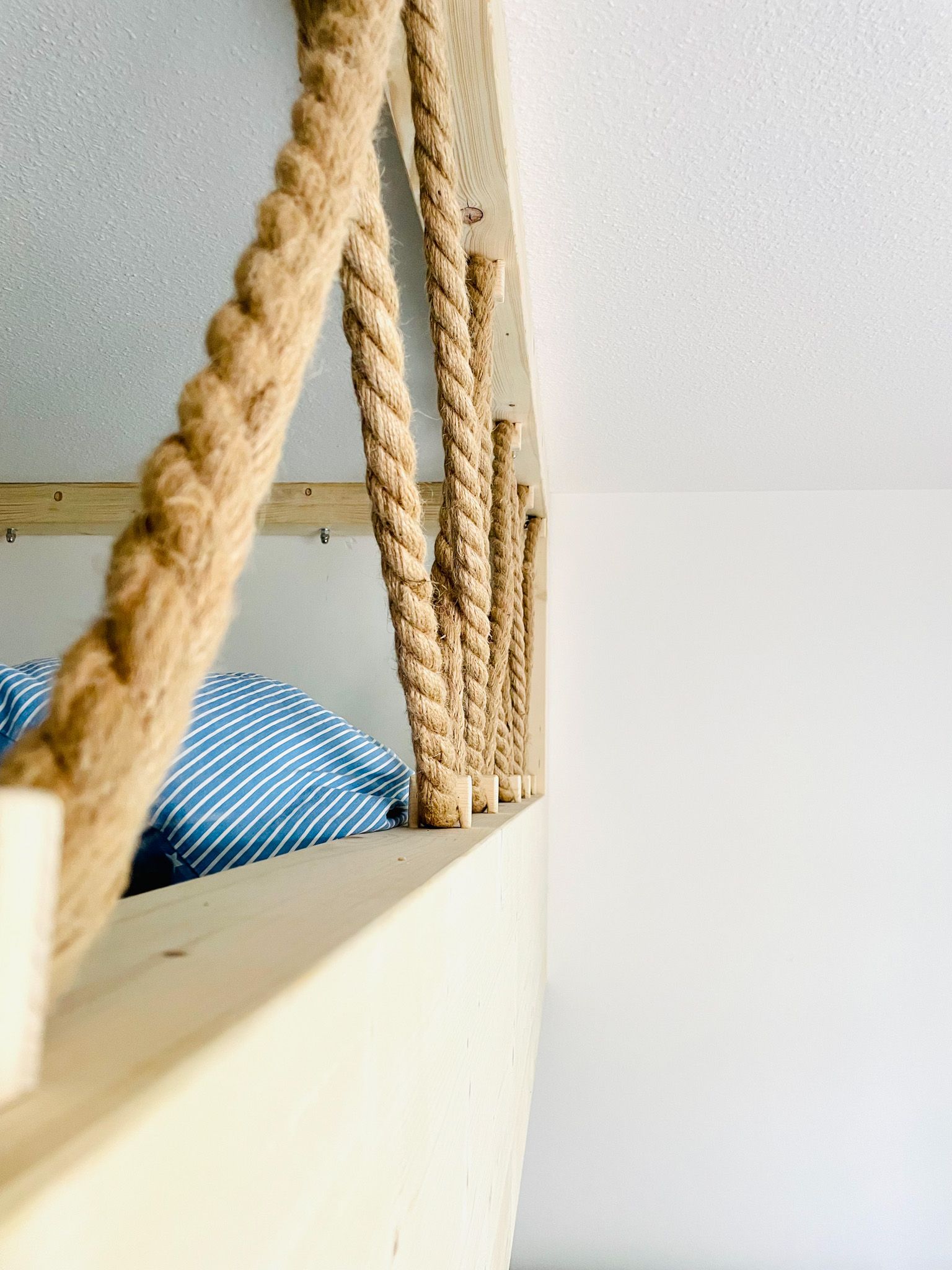 Nahaufnahme eines hölzernen Hochbetts mit Seilgeländer vor einer weißen Wand.