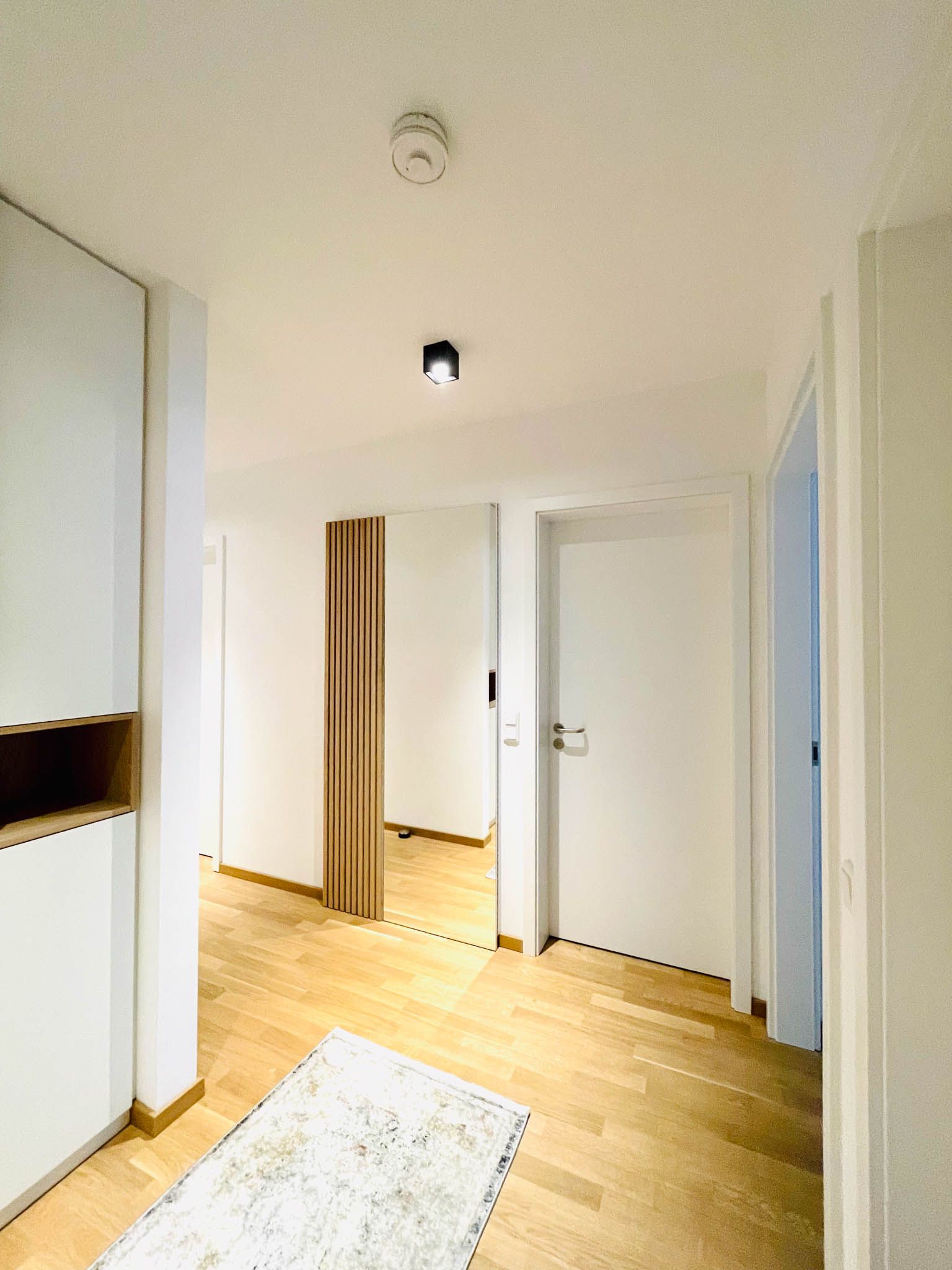 Flur mit hellem Holzboden, weißen Wänden und Türen; Teppich auf dem Boden.