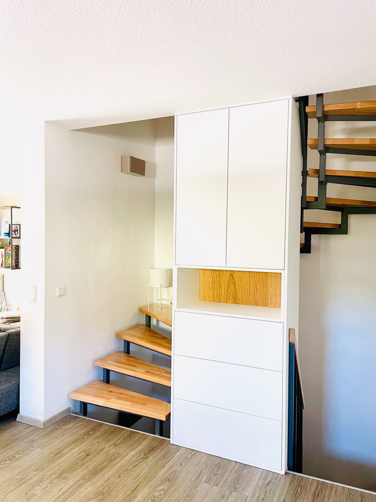 In eine Treppe eingebautes weißes Lagermöbel mit Holzstufen, Metallgeländer und hellem Holzboden.