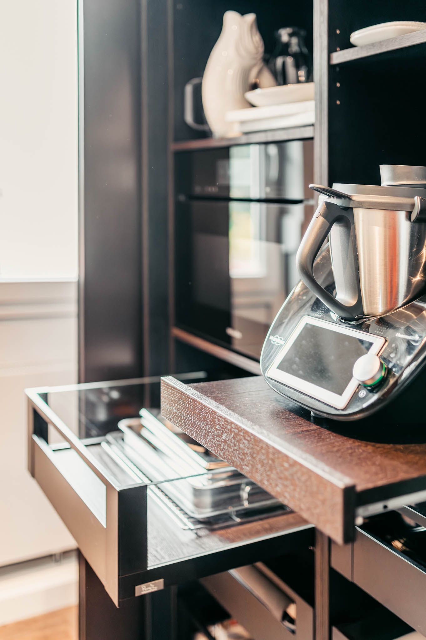 Schwarzer Küchenschrank mit einem ausziehbaren Regal, in dem sich eine Küchenmaschine befindet, und einer Schublade mit Metalltabletts.