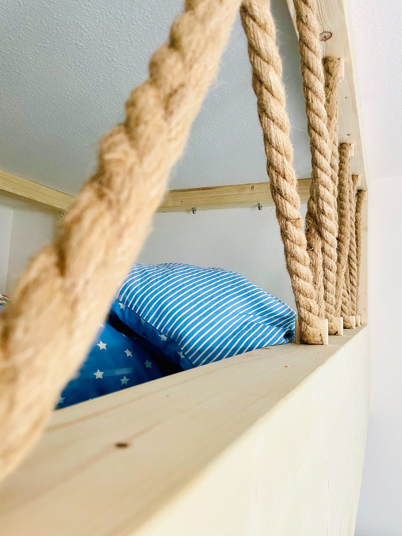 Seilgeländer an einem Kinderbett, mit blauem Kissen und Sternenaufdruck.