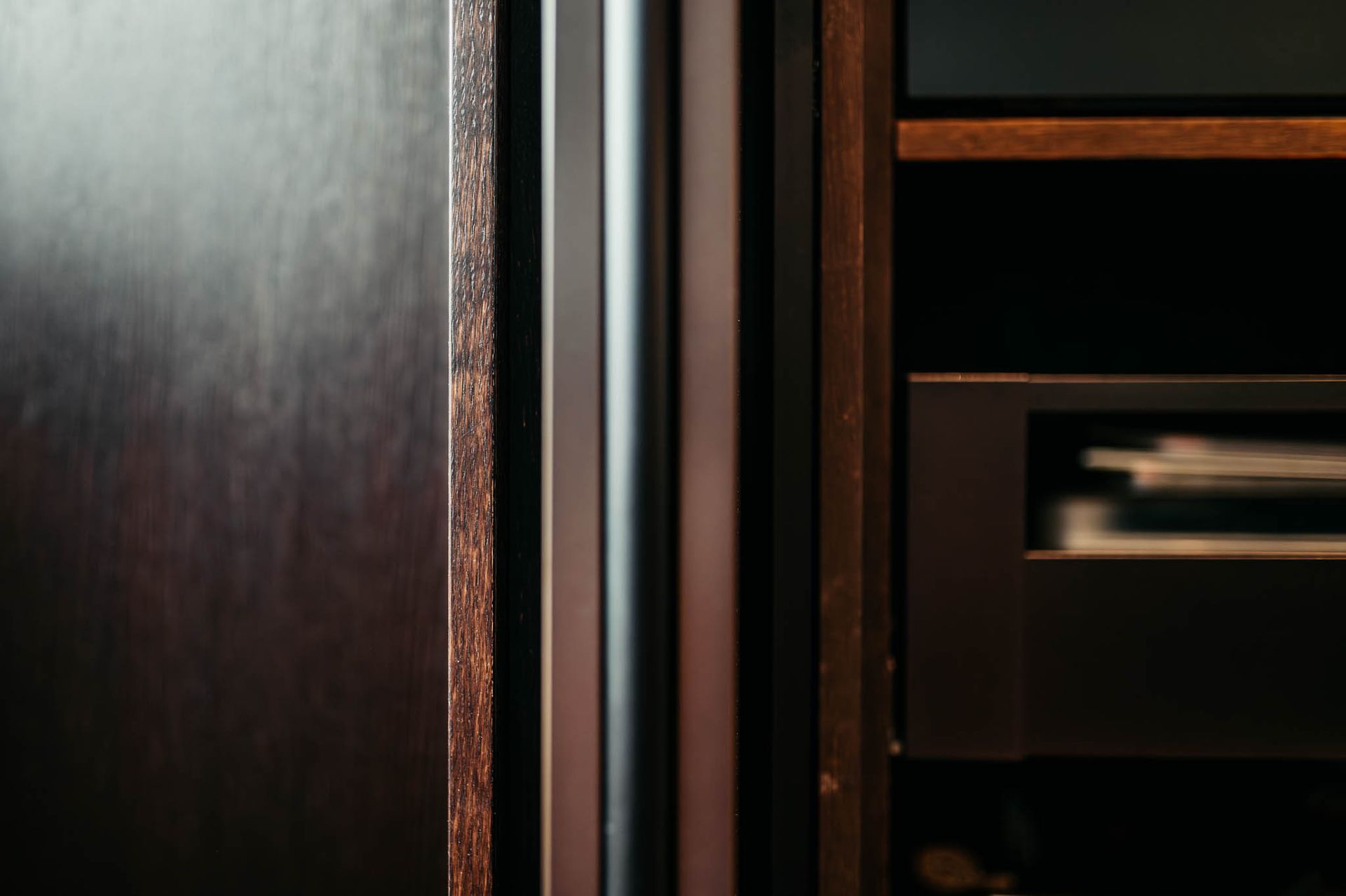 Nahaufnahme von dunklen Holzschränken mit vertikalen schwarzen Metallgriffen und Innenregalen.