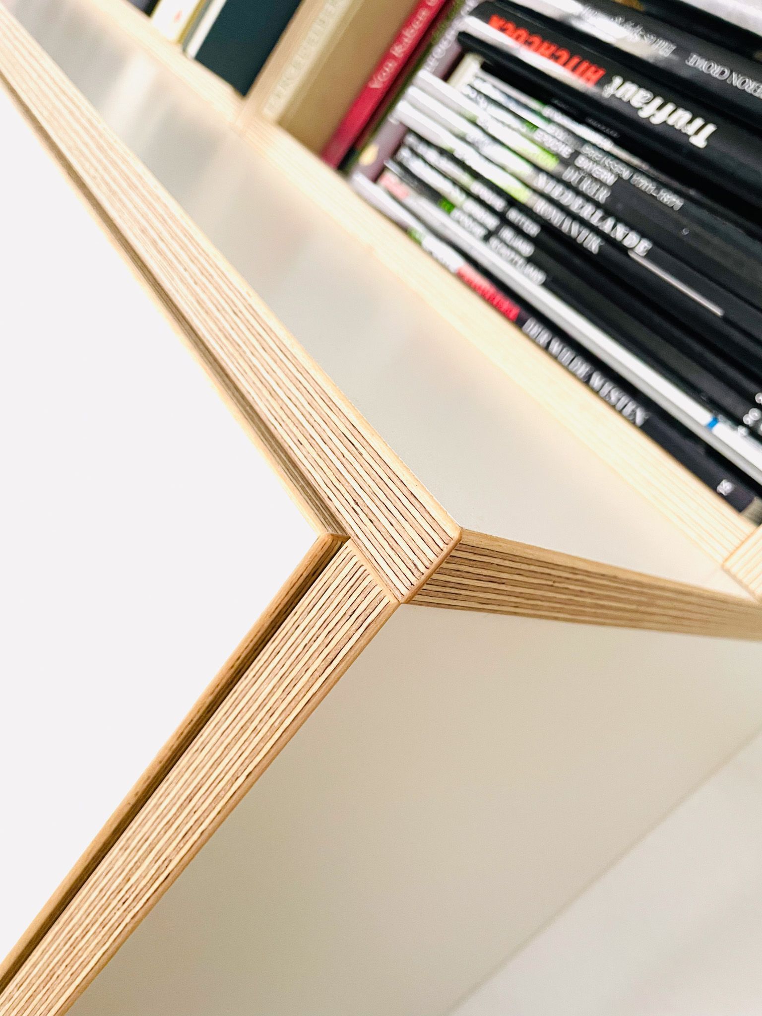 Nahaufnahme einer weißen Bücherregalecke mit wabenförmigem Rand und gestapelten Zeitschriften.