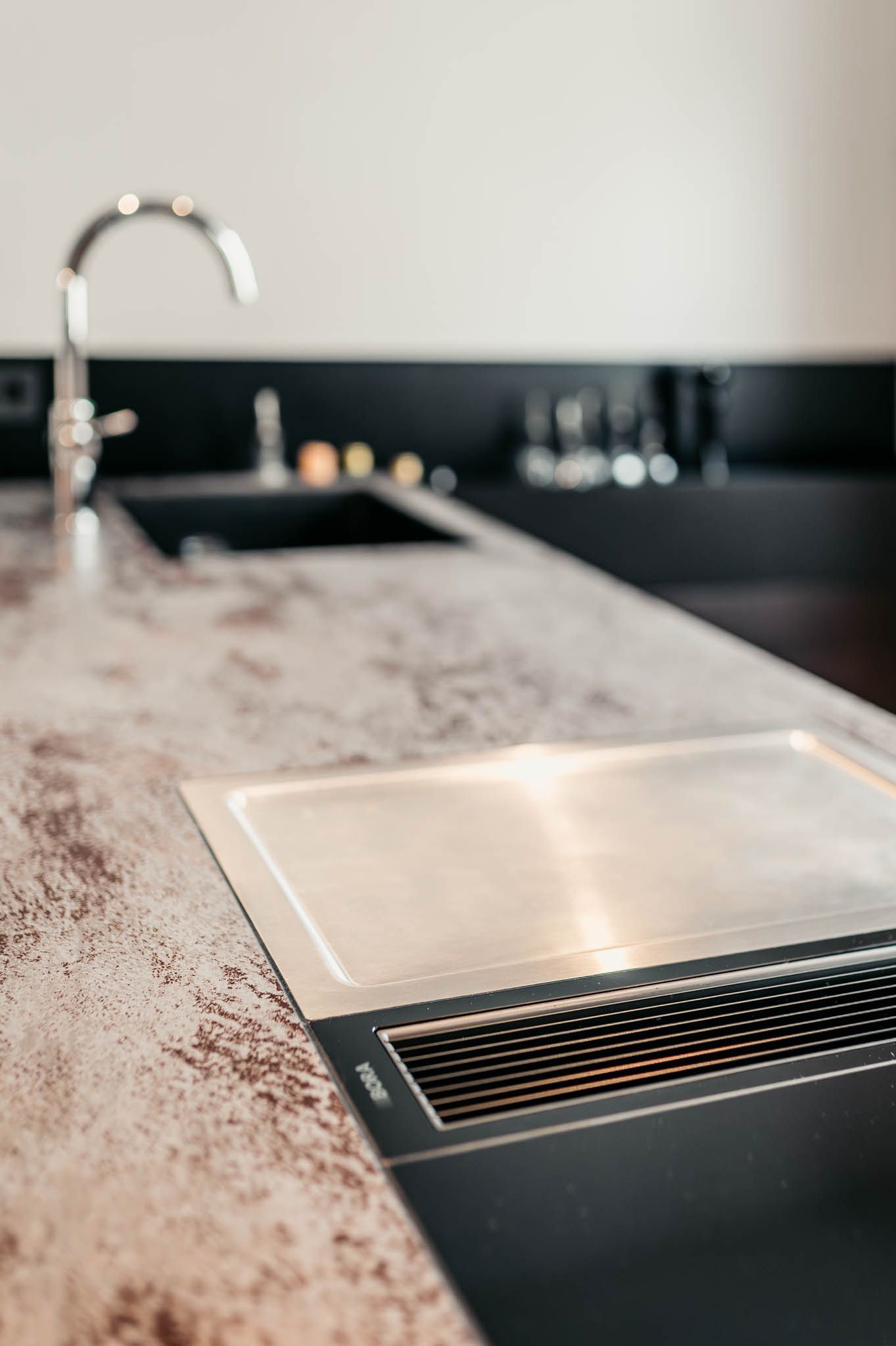Küchenarbeitsplatte mit eingebautem Kochfeld, Wasserhahn und Spüle; neutrale Töne mit Edelstahl und dunklem Finish.