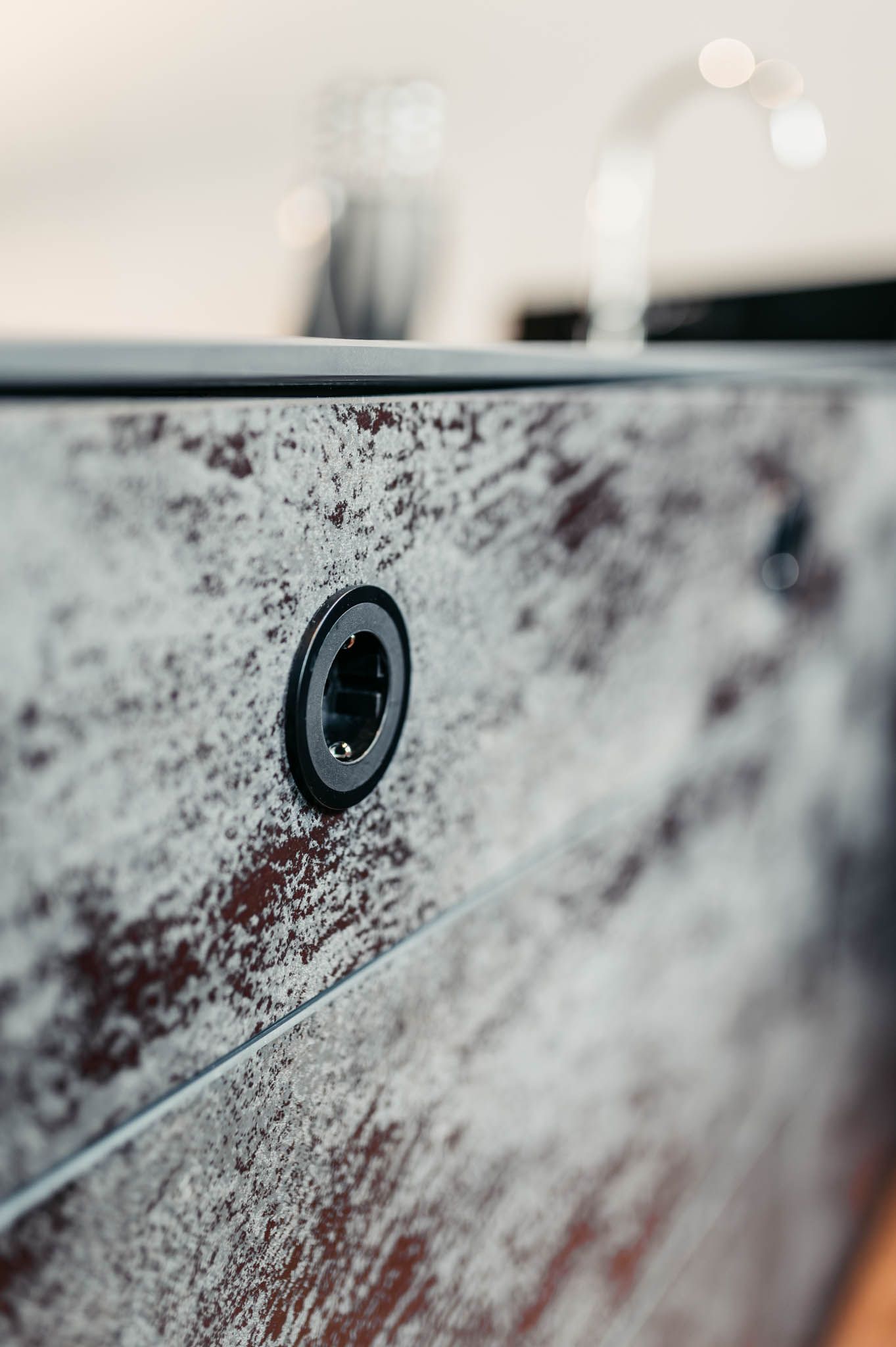 Nahaufnahme eines dunklen Schranks mit einem runden schwarzen Knopf. Verschwommenes Waschbecken und Gegenstände im Hintergrund.