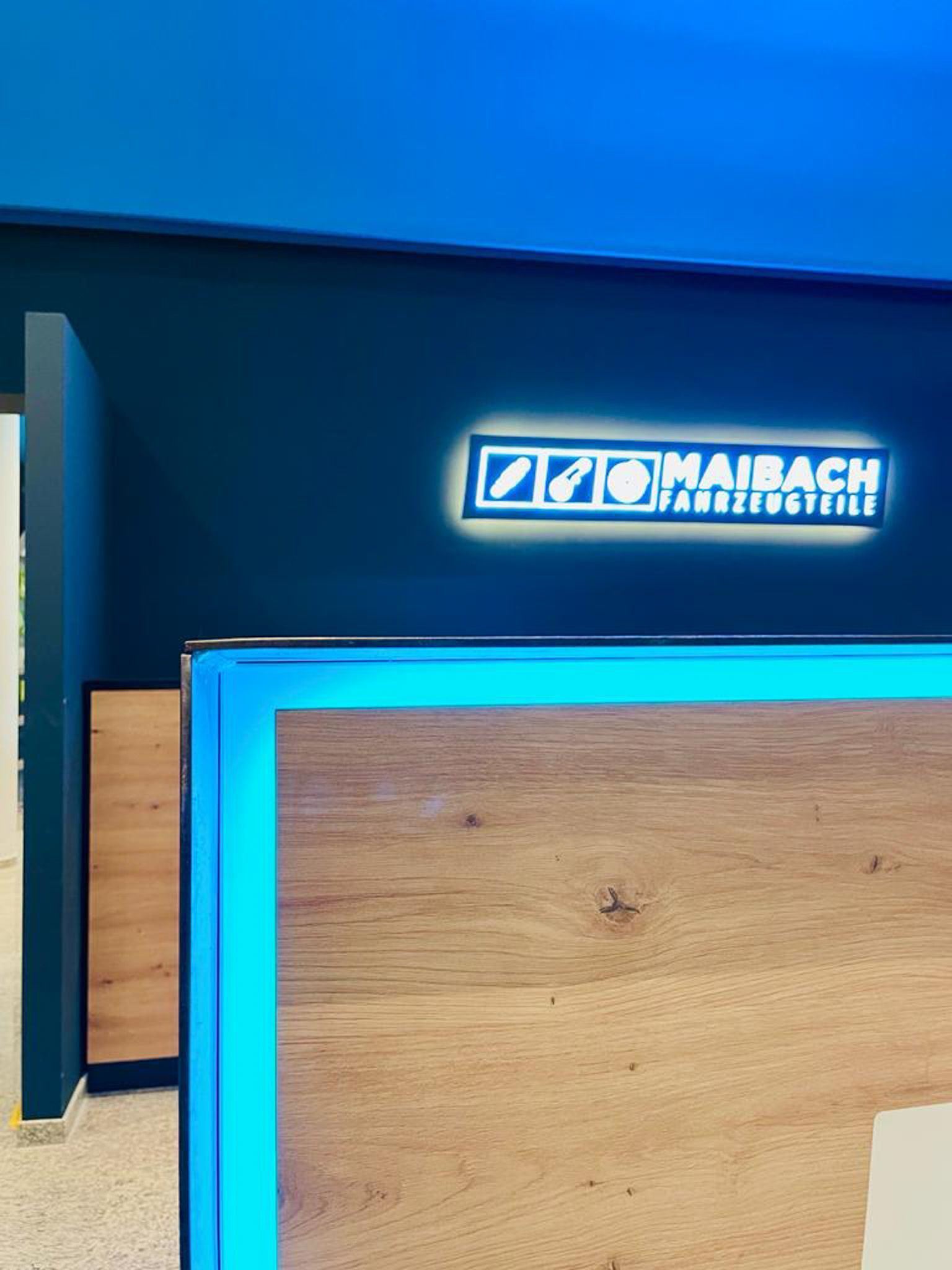 Empfangstresen mit Leuchtschrift „MAIRBACH“ darüber. Holzmaserungsfront mit blauer LED-Umrandung, vor dunkelblauer Wand.