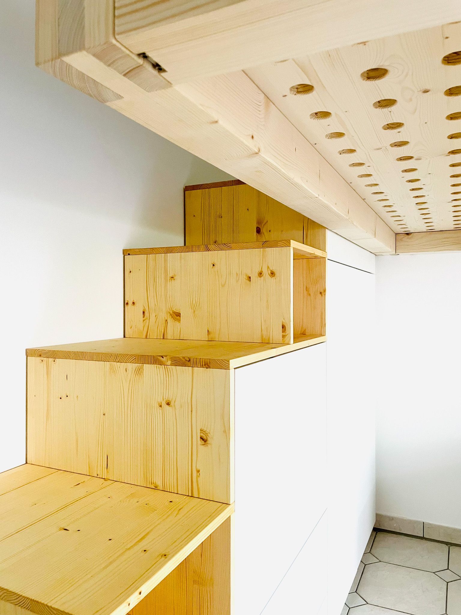 Eine Holztreppe führt hinauf zu einem Holzloft mit weißen Wänden.