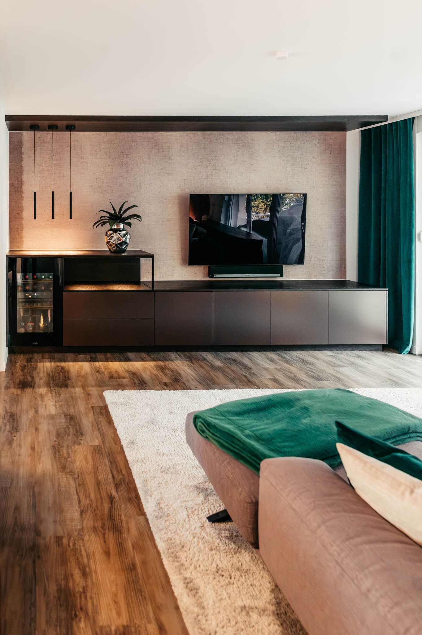 Wohnzimmer mit Fernseher auf einem dunklen Schrank, braunem Bodenbelag, grünen Akzenten und einem Teppich.