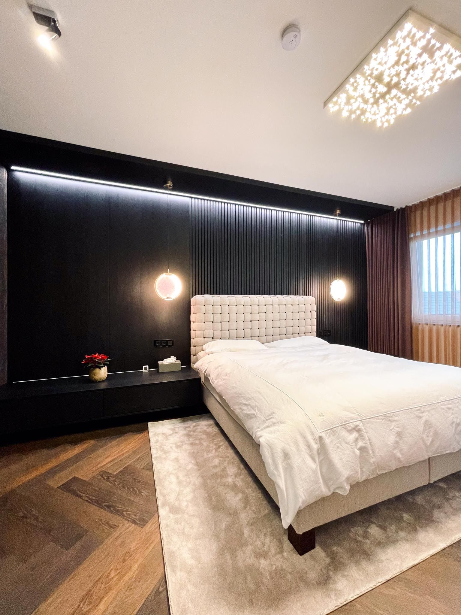 Modernes Schlafzimmer mit schwarzer Akzentwand, Bett, Teppich und dekorativer Beleuchtung.