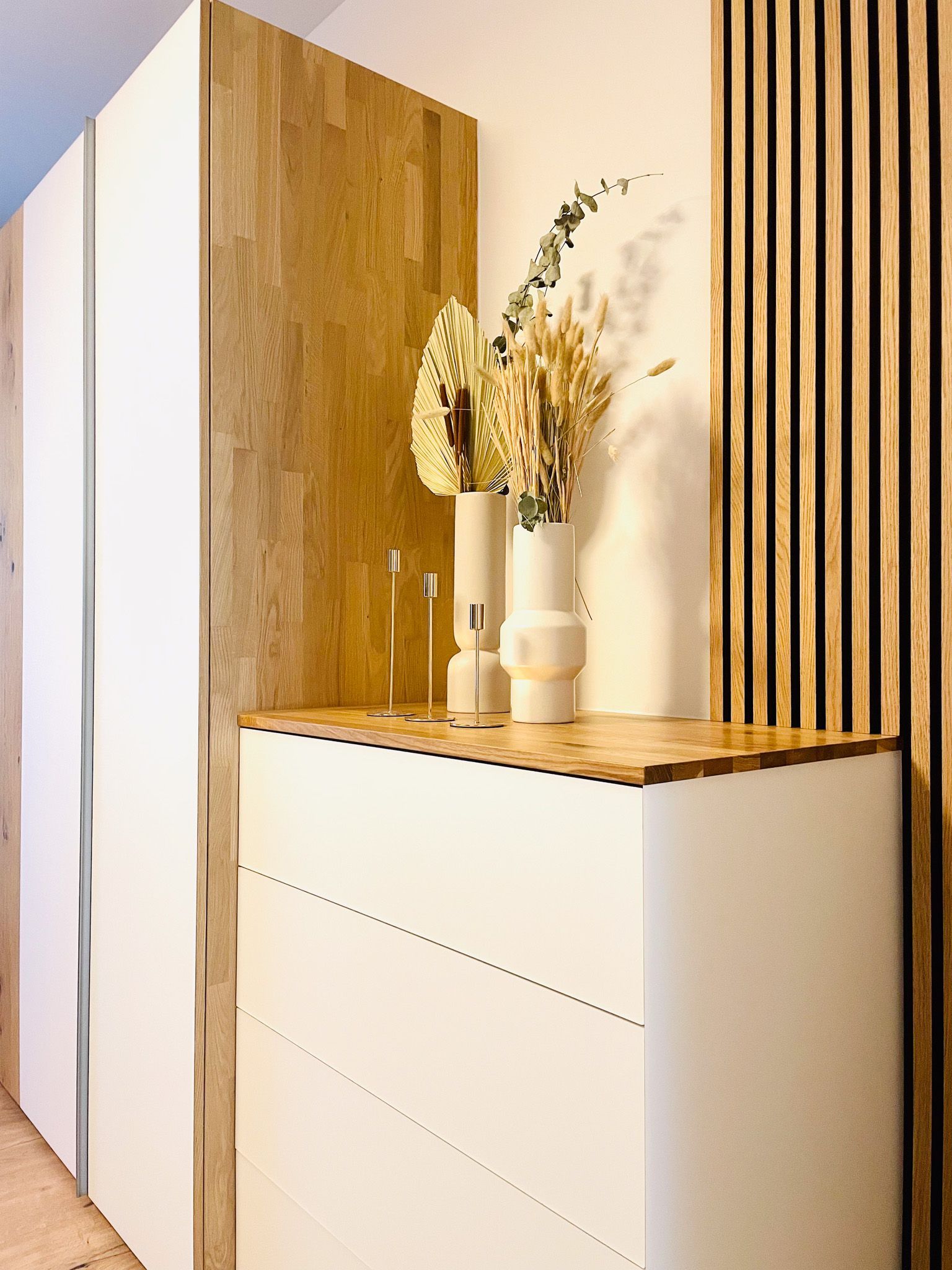 Weiße Kommode mit Holzarbeitsplatte und Akzenten, darauf Vasen und Trockenblumen.