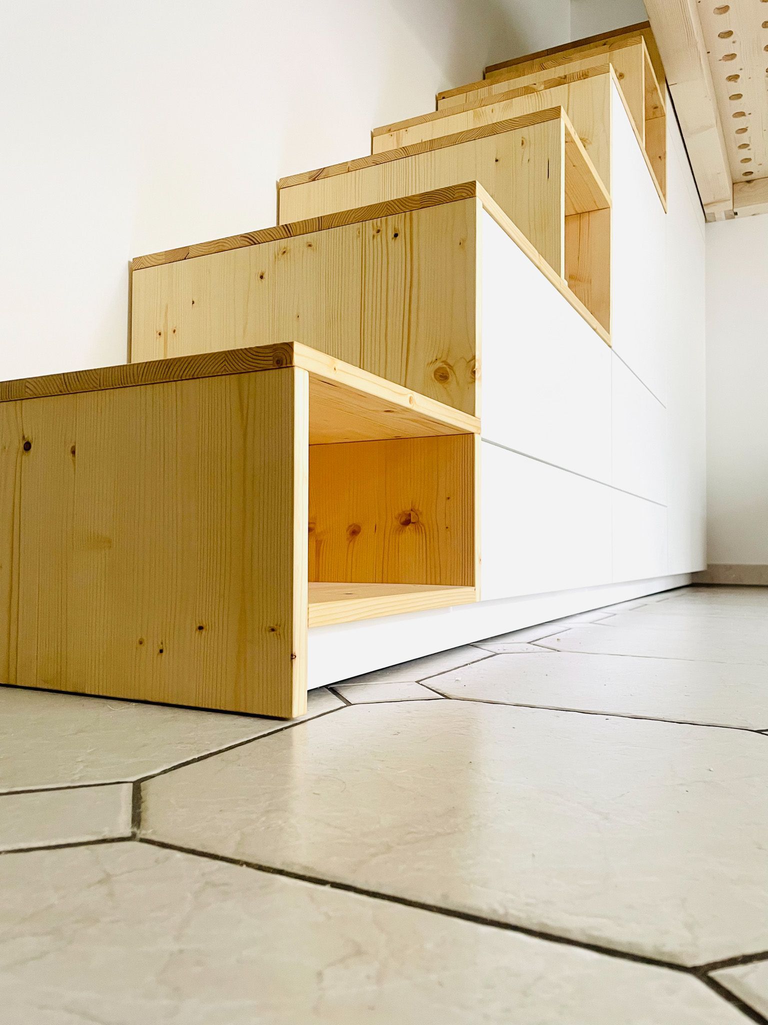 Holztreppe mit eingebauten Ablagefächern, weißer Wand und geometrischem Fliesenboden.