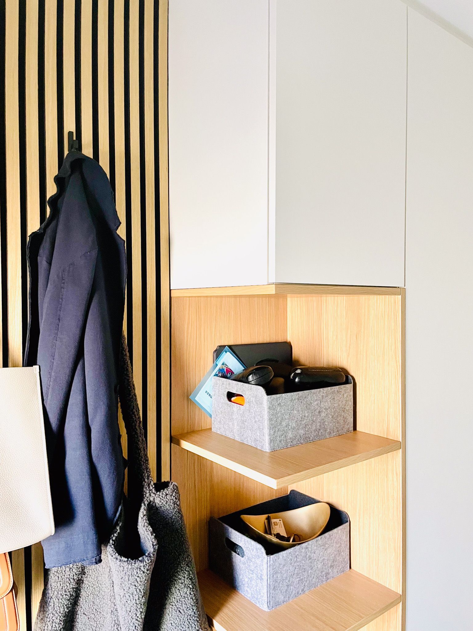 Holzregal mit Aufbewahrungsboxen, einem Mantel und einer Tasche in einer Ecke.