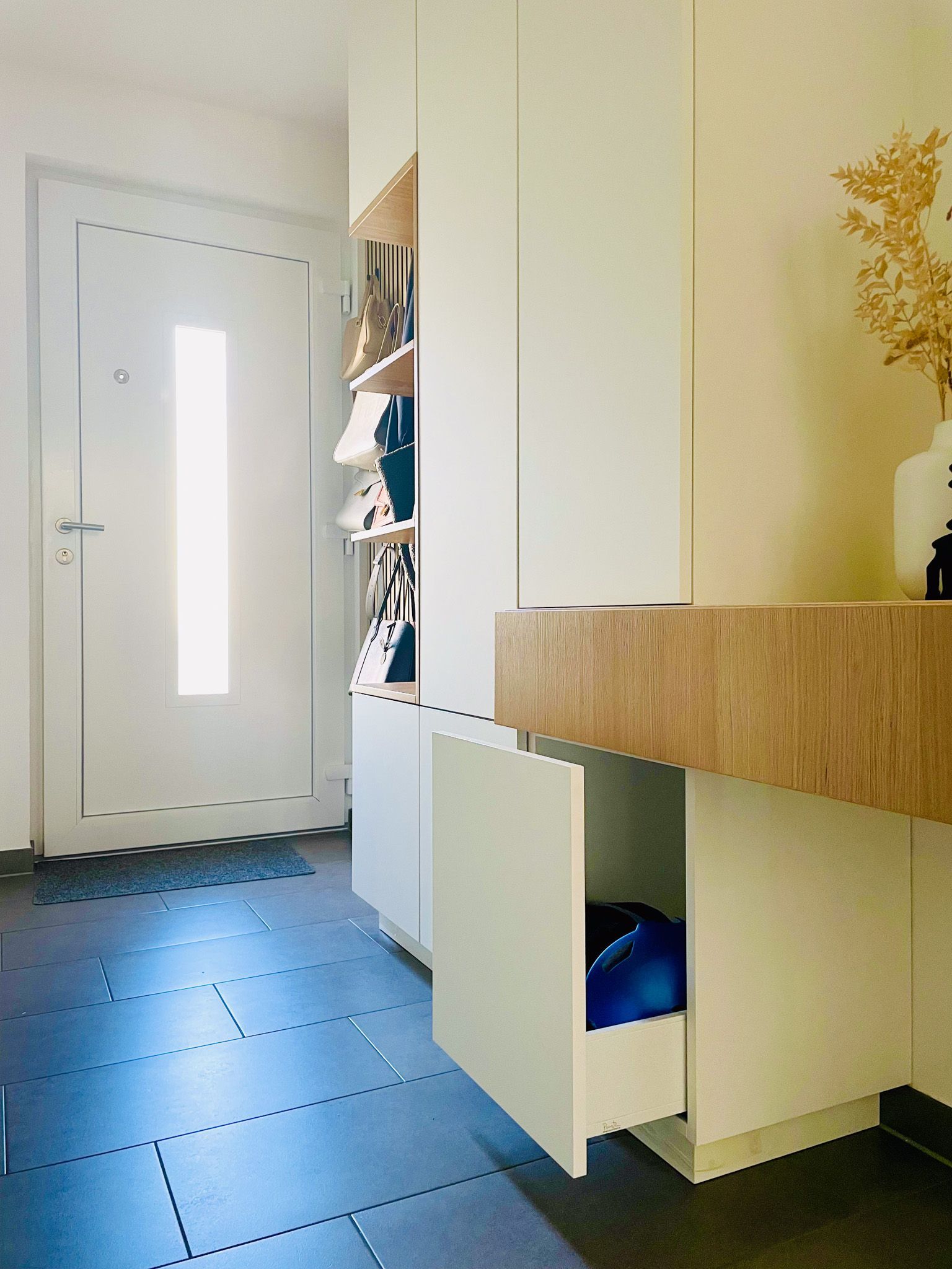 Eingangsbereich mit einem weißen Schrank, Schuhregal und einer offenen Schublade mit einem blauen Ball darin.