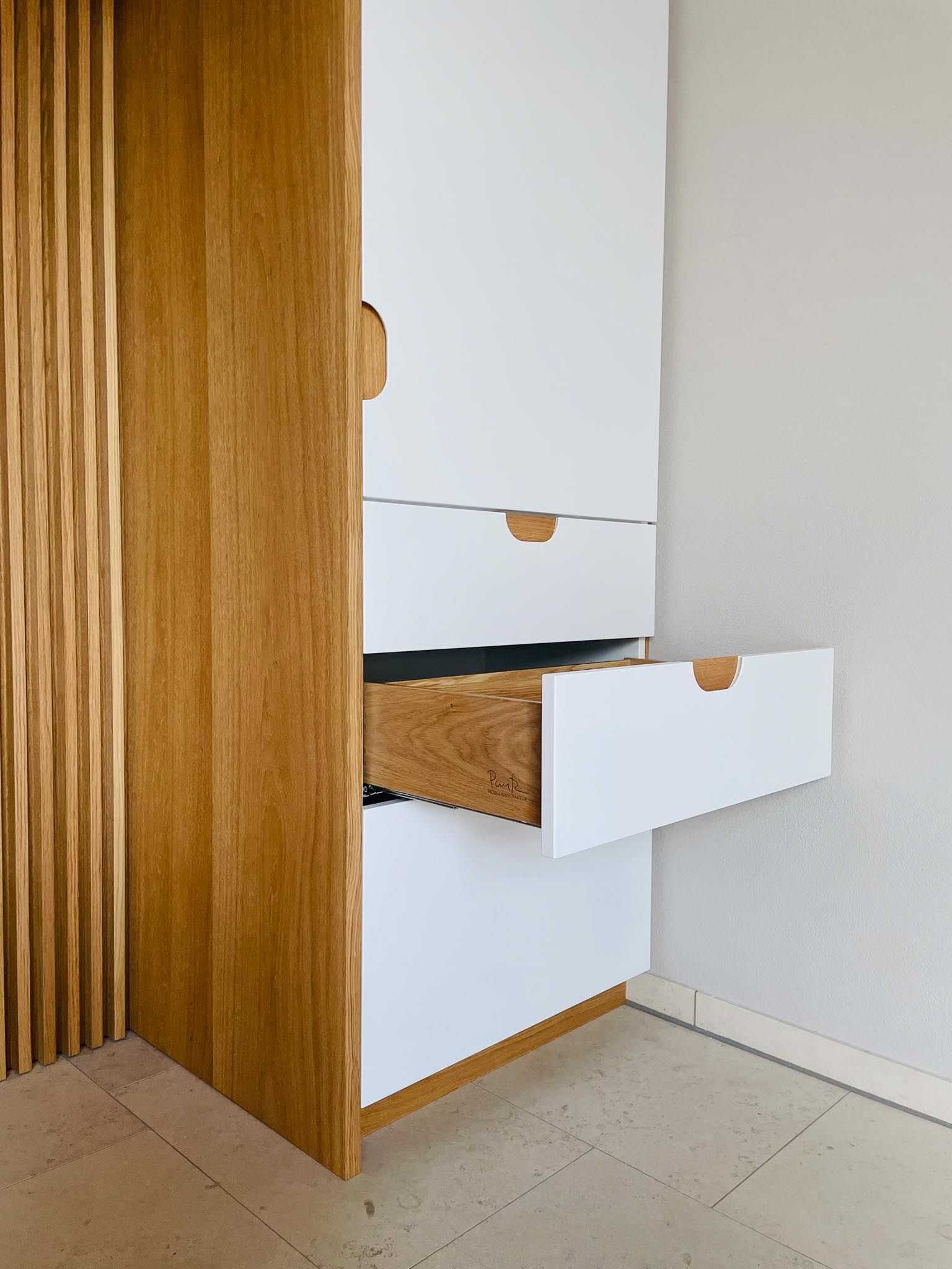 Weißer Schrank aus Holz mit offener Schublade in einer Ecke, mit sichtbarem Innenleben und Griffen.